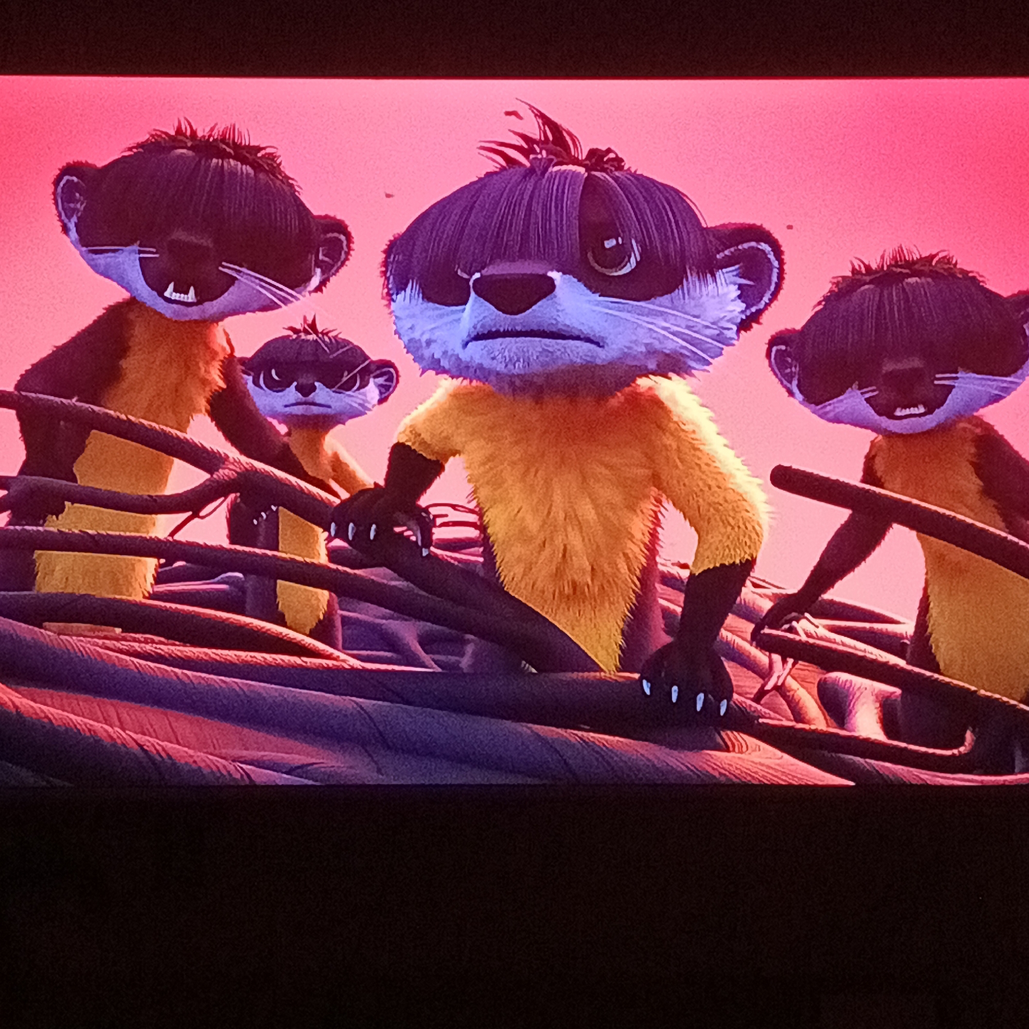 The image shows a group of animated ferret-like creatures with dark brown hair and yellow-orange fur, standing on a structure made of interwoven dark ropes or branches. The creatures appear to be in a state of alertness or concern, with the central character exhibiting a frown. The background is a solid red color. The style suggests a frame from a CGI animated film or television show. The city of Марковский, Russia is not present or indicated in the provided visual information.