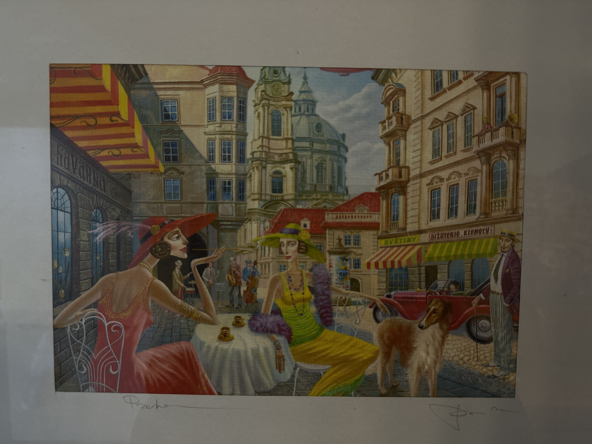 The image depicts a cityscape scene with two women seated at a table outside a cafe. The woman on the left is wearing a red dress and a large red hat, while the woman on the right is wearing a yellow dress, a green hat, and a purple shawl. They are seated at a white table with cups on it. Behind them are buildings, including a building with a dome that resembles St. Nicholas church of Stara Zagora, Bulgaria. There is also a man standing next to a red vintage car and a dog. In the background, there are musicians playing instruments.