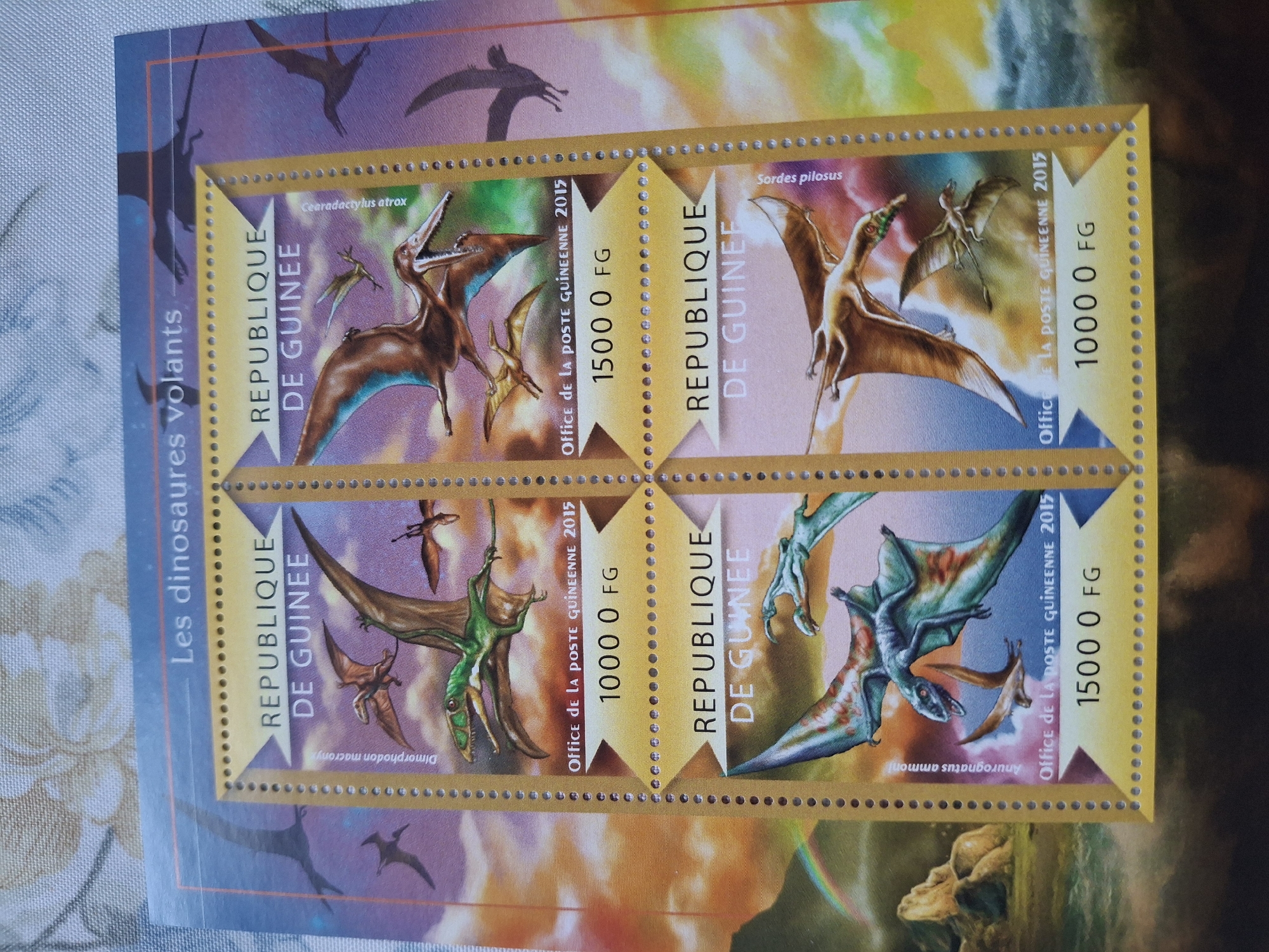 The image shows a block of stamps featuring flying dinosaurs. The stamps are from the Republic of Guinea and commemorate the "flying dinosaurs". Each stamp depicts a different flying dinosaur species and is valued at either 1000 or 1500 FG. The dinosaur species labeled are: Cearadactylus atrox, Sordes pilosus, Dimorphodon macrony, and Anurognatus ammoni. The stamps are dated 2015. The overall background of the stamp block has other blurred images of flying dinosaurs. The image does not appear to be located in Pleven, Bulgaria, as the stamps originate from the Republic of Guinea.