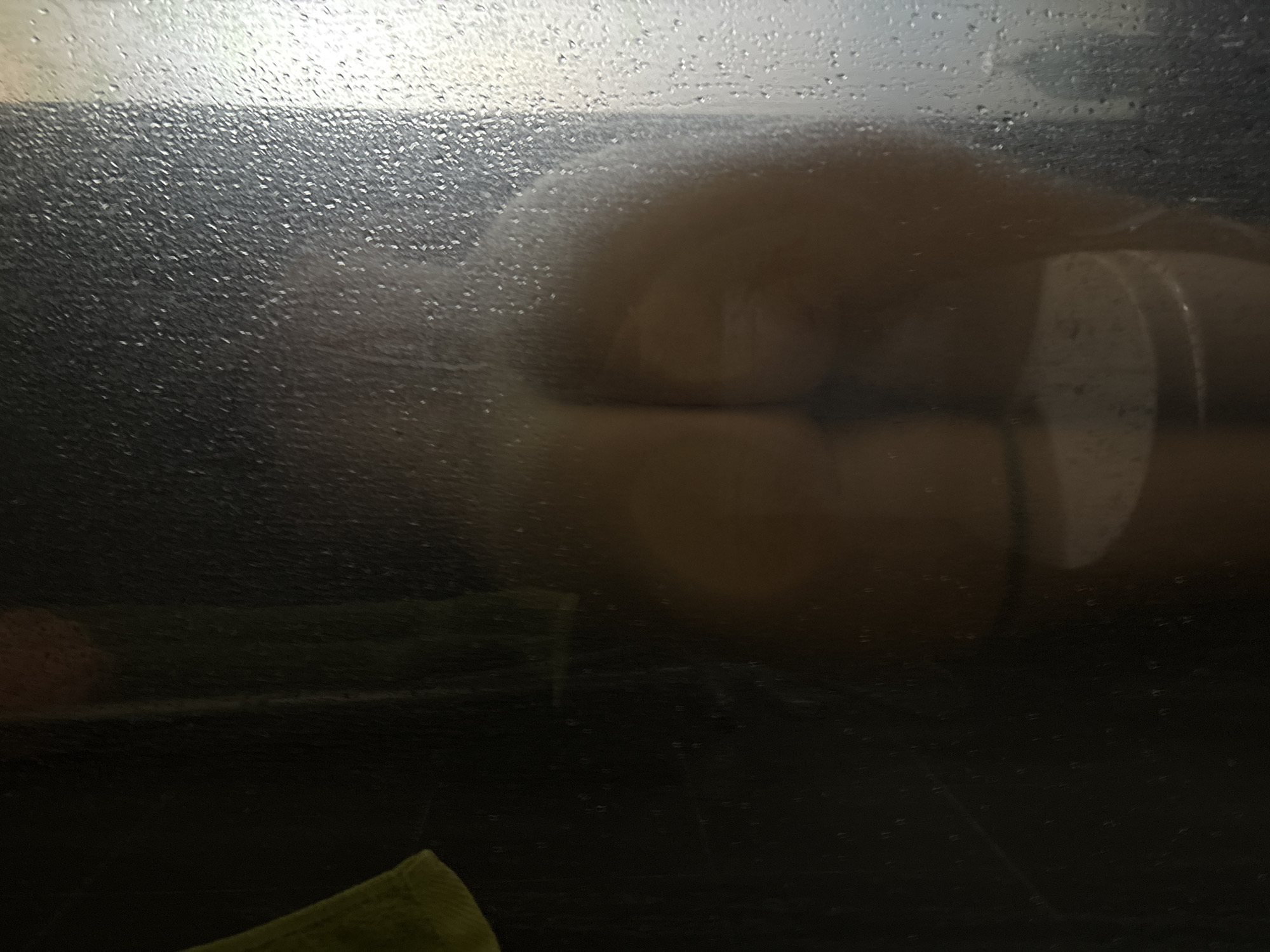 The image depicts a close-up view of a person's buttocks, partially obscured by condensation on a glass surface. The lighting is dim, creating a diffused glow that highlights the curves of the body. The condensation droplets on the glass are prominent, some appearing as small beads and others forming streaks. The lower portion of the image shows a dark, indistinct background, with a hint of a green object in the bottom left corner, possibly a towel or cloth. The overall impression is intimate and suggestive, with the condensation adding a sense of moisture and privacy. There is no visible text in the image. The scene appears to be indoors, possibly a bathroom, given the presence of condensation. The time of day and weather conditions are not discernible. The emotional tone conveyed is one of sensuality and perhaps vulnerability. The location context of Đà Nẵng, Vietnam, does not provide specific visual cues within the image itself.