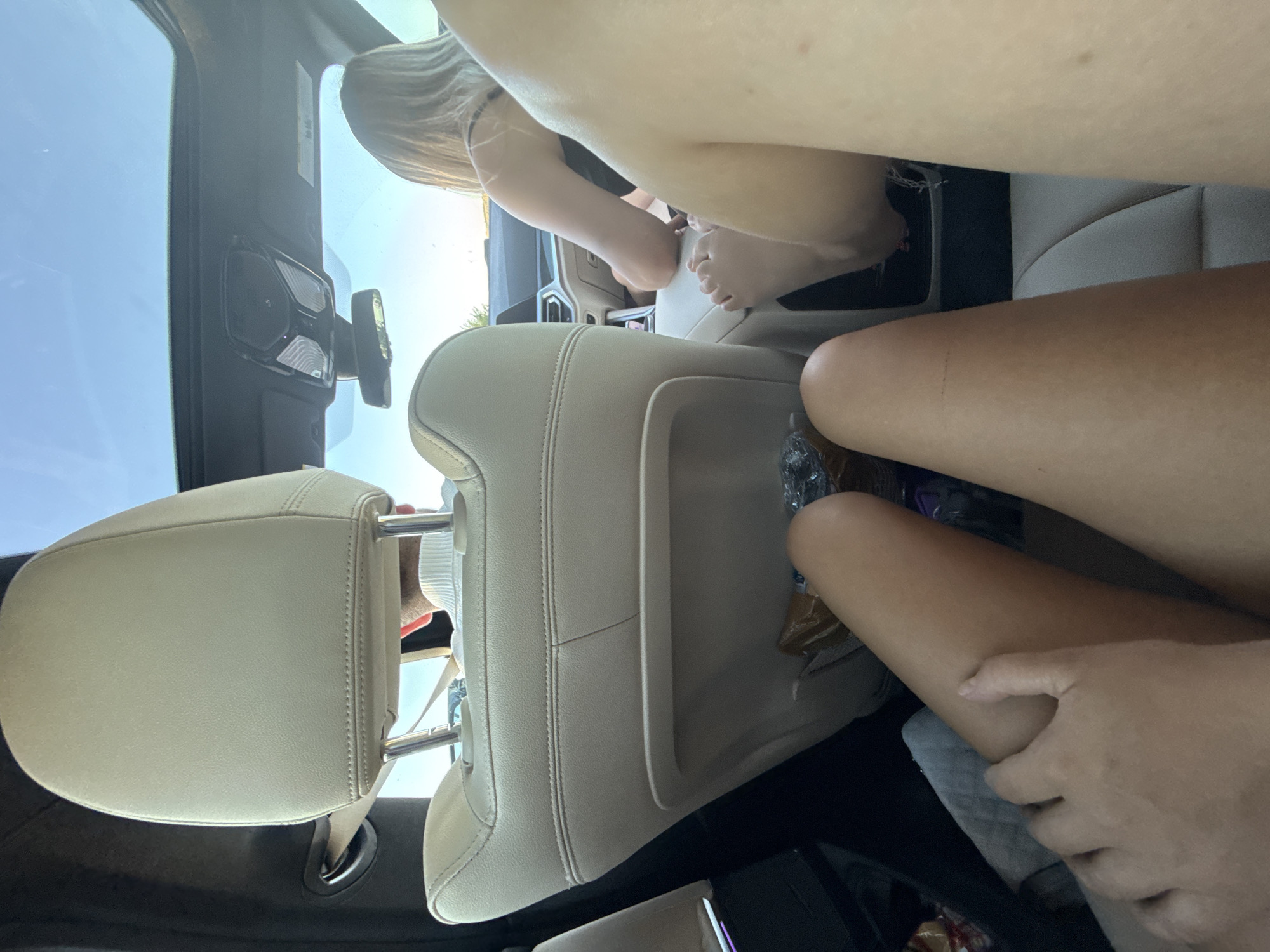 In Vozneseni, Moldova, this image captures the interior of a car with a sunroof, looking forward. Two individuals are visible: a person in the driver's seat with blonde hair, wearing a black top, and another person in the passenger seat partially obscured, wearing a white turtleneck. In the foreground, the legs of two other individuals are in view. The seats are upholstered in light-colored leather. A snack bag is on the floor in the rear.