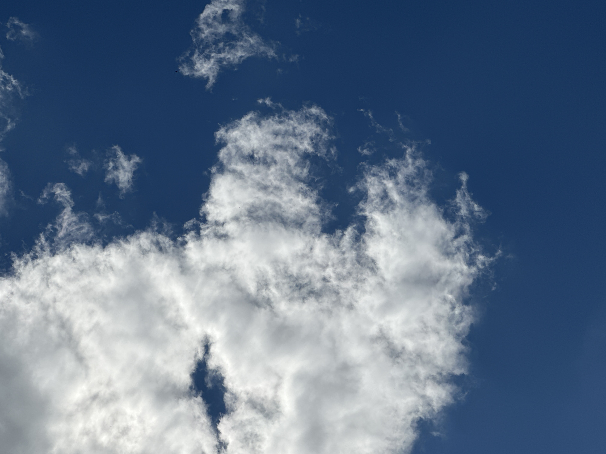 The image shows a clear blue sky with scattered white clouds. The clouds are mostly in the upper left portion of the image, with some smaller clouds dispersed throughout the sky. There is no visible indication of the city of Luhansk, Ukraine, or any people, subjects, objects, or actions. The environment is solely composed of the sky and clouds.