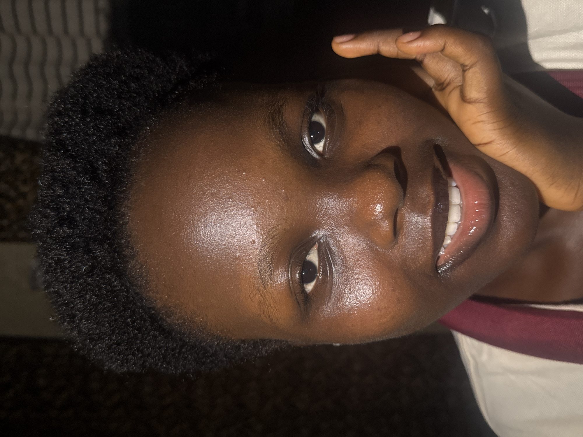 A close-up portrait shows a person with dark skin and short, dark hair smiling slightly and looking directly at the camera. One hand is visible near the face. The background is dark and indistinct. There is no information in the image to identify that the photograph was taken in Onitsha, Nigeria.