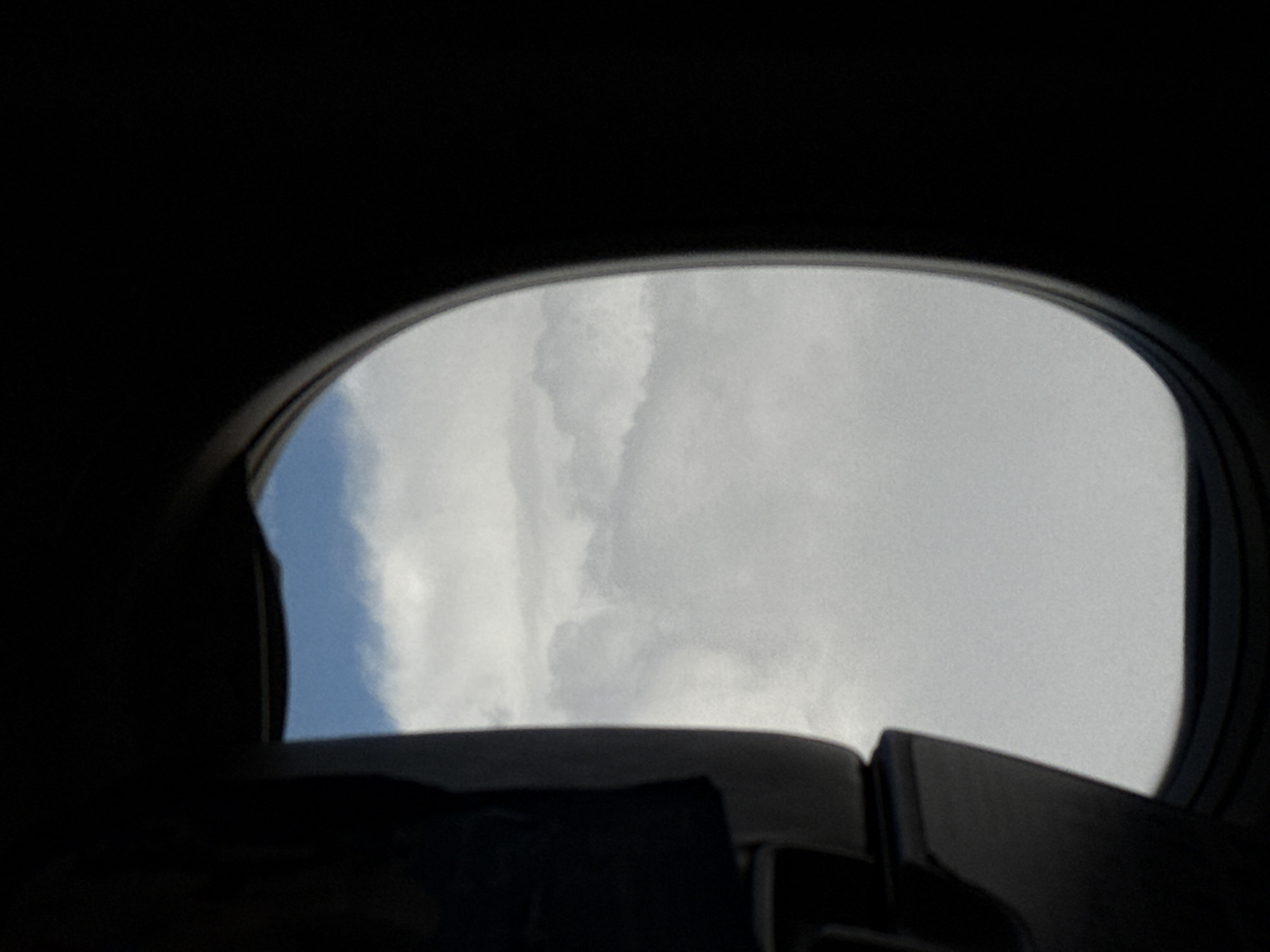 The image shows a view of the sky with clouds through an opening in what appears to be a structure, possibly a sunroof or window. The sky is partly blue, and partly covered with white clouds. The opening is surrounded by a dark, possibly black, material. The image is taken from inside a dark space, possibly a vehicle or building. The location is not discernible from the image itself and cannot be determined to be in Khimki, Russia, without additional context or information.