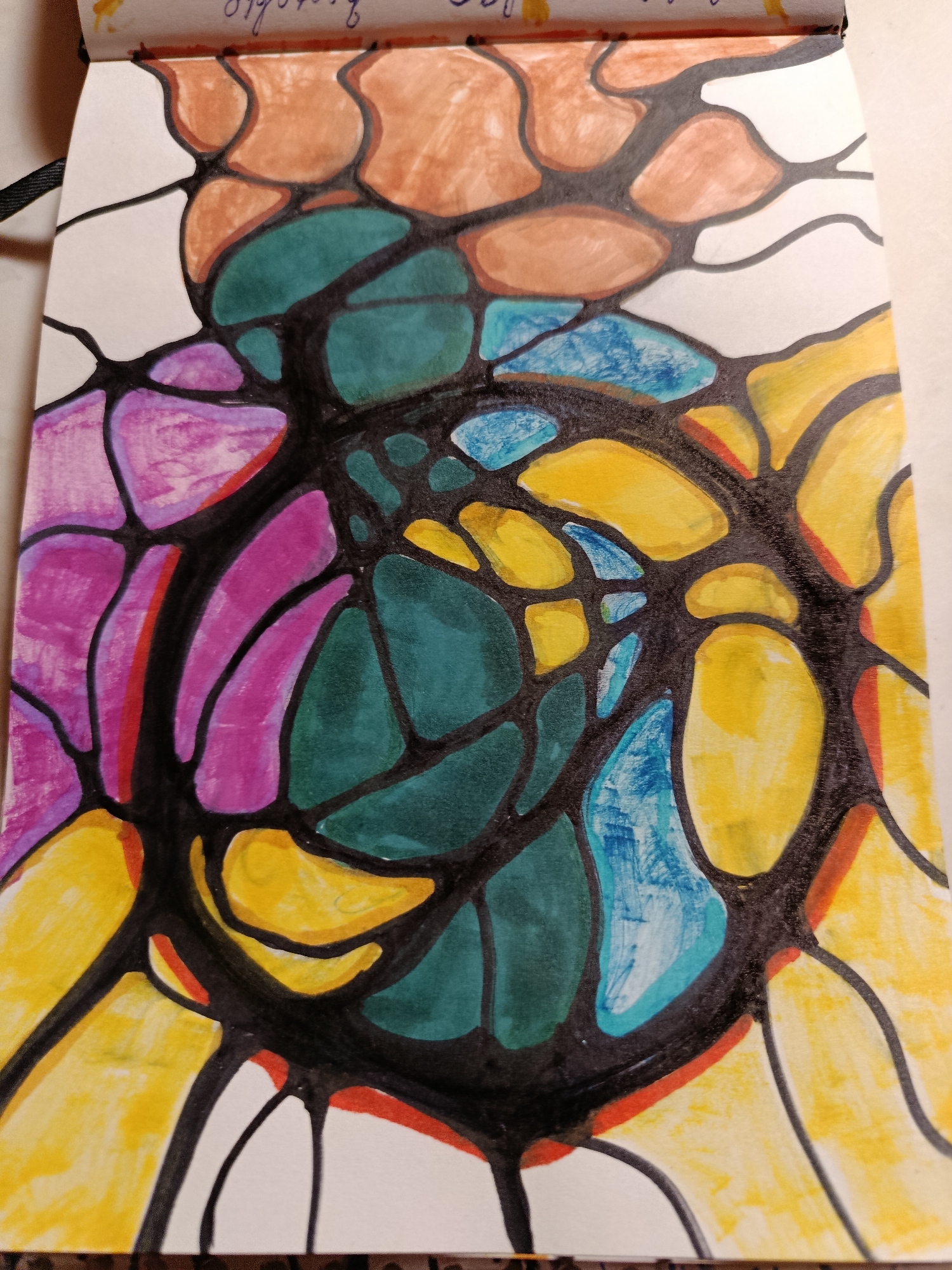 An abstract drawing on paper is depicted. The drawing features a network of irregular black lines that divide the paper into various cells. These cells are filled with different colors, including brown, green, purple, yellow, and blue. Some cells remain white. The drawing appears to be in a sketchbook, as indicated by the binding visible at the top. The background of the image is a plain white surface. There are no people or identifiable locations within the image.