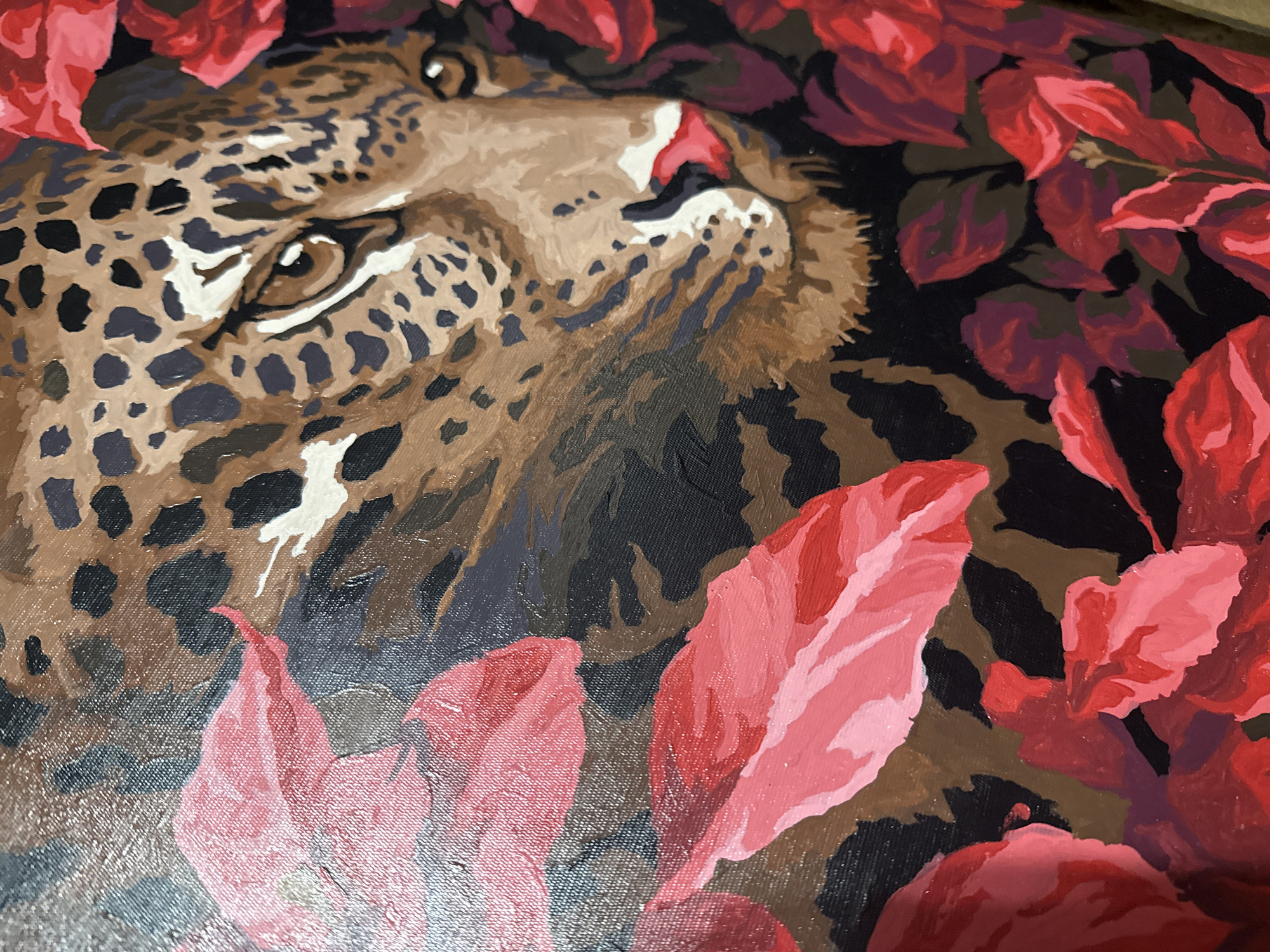 A close-up painting shows a leopard surrounded by red leaves. The leopard's head is angled, with an eye visible and spots covering its fur. The leaves are a mix of shades of red, arranged around the leopard's face and body. The background has areas of black and brown, adding depth to the painting.