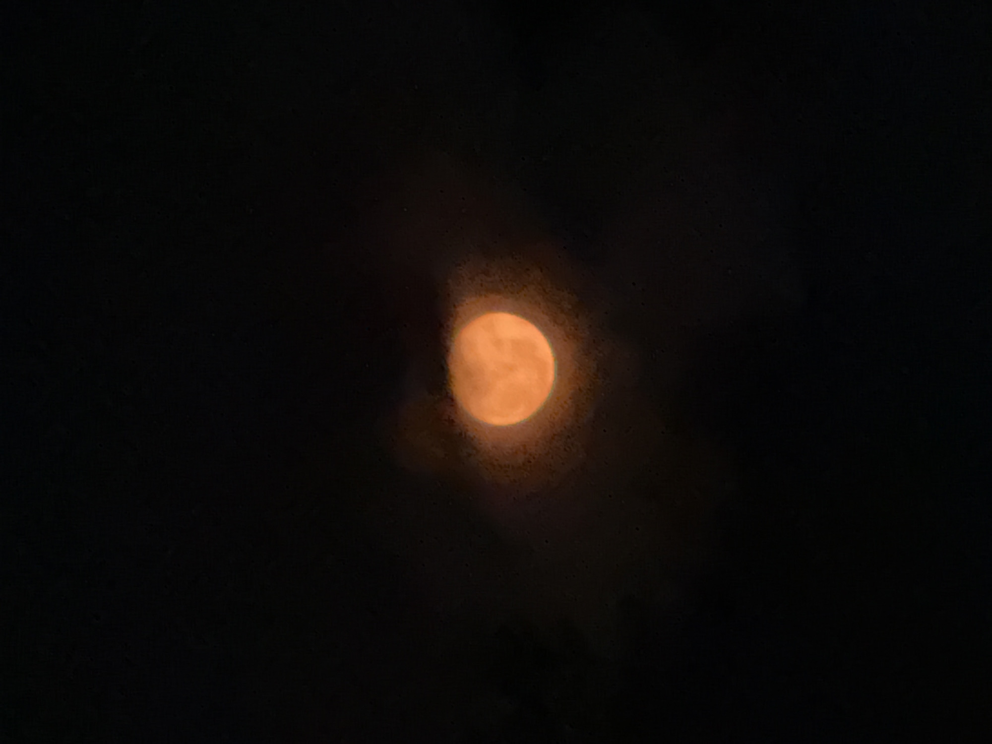 An orange moon is centered in the frame against a dark night sky. The moon's light is diffused, suggesting it is partially obscured by clouds or atmospheric conditions.
There are no people visible in this image. It is difficult to determine the specific location within Oaxtepec based on this single photograph. Further contextual information or details in the wider surroundings are needed to determine the location.