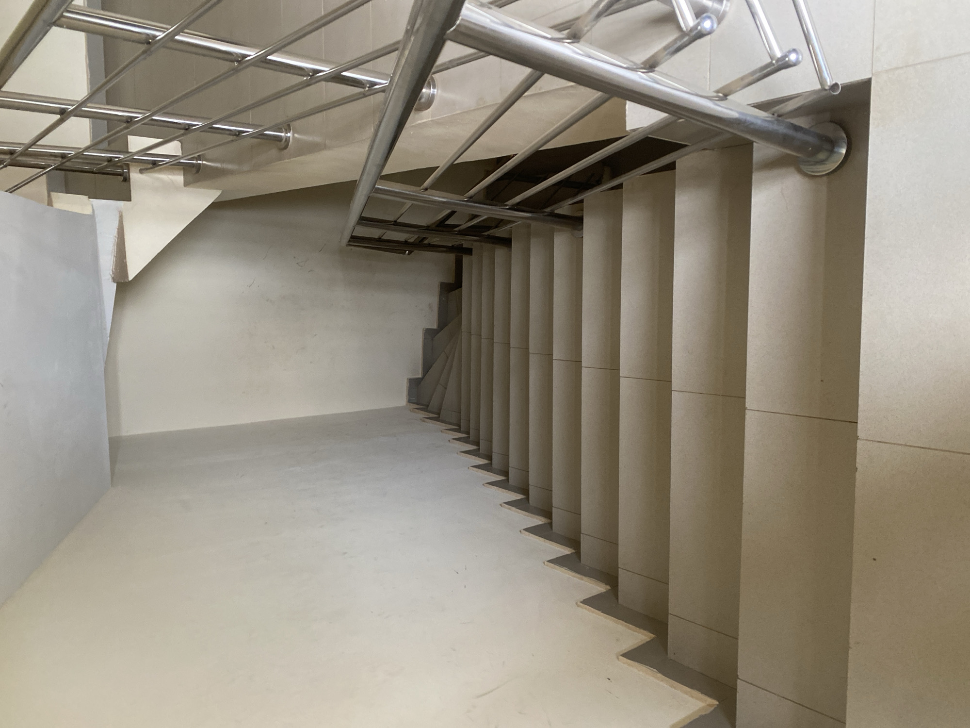 A downward angle shot reveals a staircase within a building. The stairs are constructed of a light, beige-colored stone or tile. A metal railing runs along the side of the staircase. The surrounding walls are painted a light, neutral color. The floor at the bottom of the stairs is a similar light color. There is no one visible in the scene, and no actions or interactions are occurring. The location of the image is likely a modern building, possibly a commercial or residential space, but the specific location in Abuja, Nigeria, cannot be determined from the image.