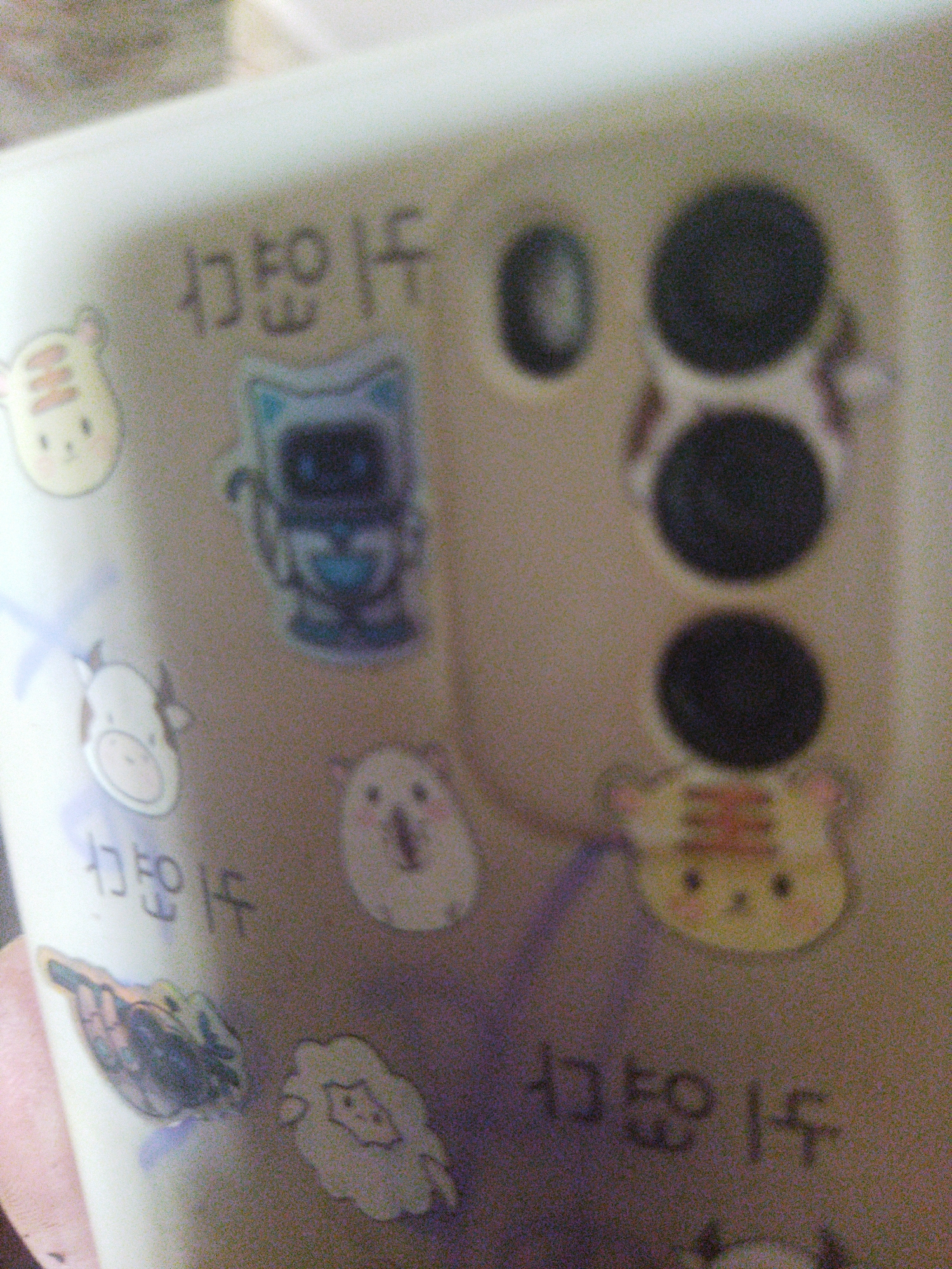 The image shows a close-up of a phone case decorated with cartoon stickers and Korean text. The case is light-colored and features a camera array with three large lenses and a smaller one. Various cartoon stickers, including a tiger, robot, cow, hamster, and sheep, are scattered across the case. Korean text is also visible in several places. The image does not provide information to identify a location in Kramatorsk, Ukraine, or any other specific location.