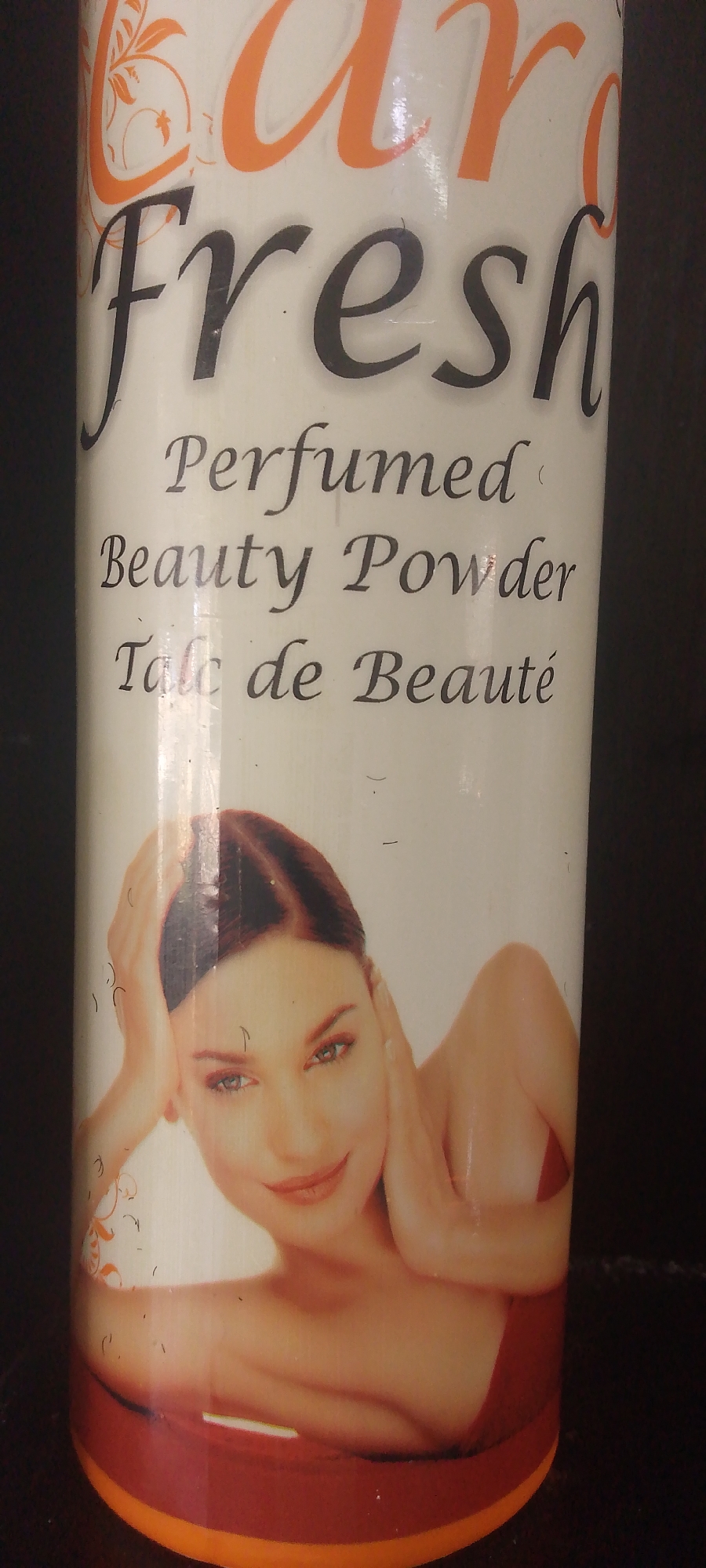 The image shows a close-up of a cylindrical container of "Pure Fresh Perfumed Beauty Powder" and "Talc de Beauté". The container features an illustration of a woman's face and upper body with her hands near her head. The background is dark, suggesting the container is indoors or in a dimly lit area. There are no discernible landmarks or contextual elements that would allow for the identification of a specific location within Jalingo, Nigeria. The image focuses solely on the product packaging.