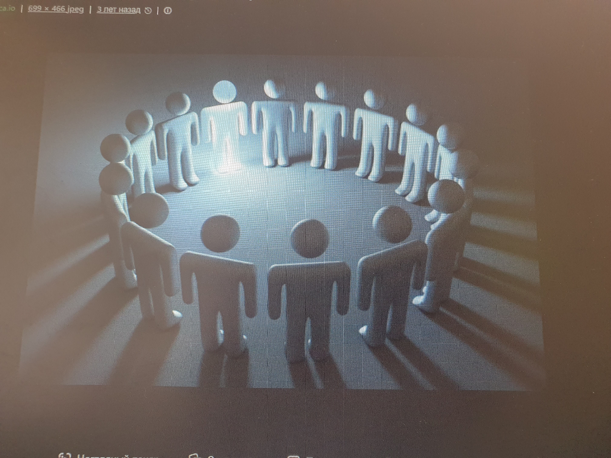 The image shows a 3D rendering of a group of stylized human figures arranged in a circle. The figures are simplistic, with rounded heads and blocky bodies, and are all the same pale blue color. They appear to be standing on a smooth, reflective surface, casting long shadows. The lighting is dramatic, with bright highlights on the figures and a darker, shadowed background. There is no discernible location in the city of Tashkent, Uzbekistan, or any other specific geographical setting. The image is likely a digital illustration or a stock photograph representing concepts like unity, community, or teamwork.