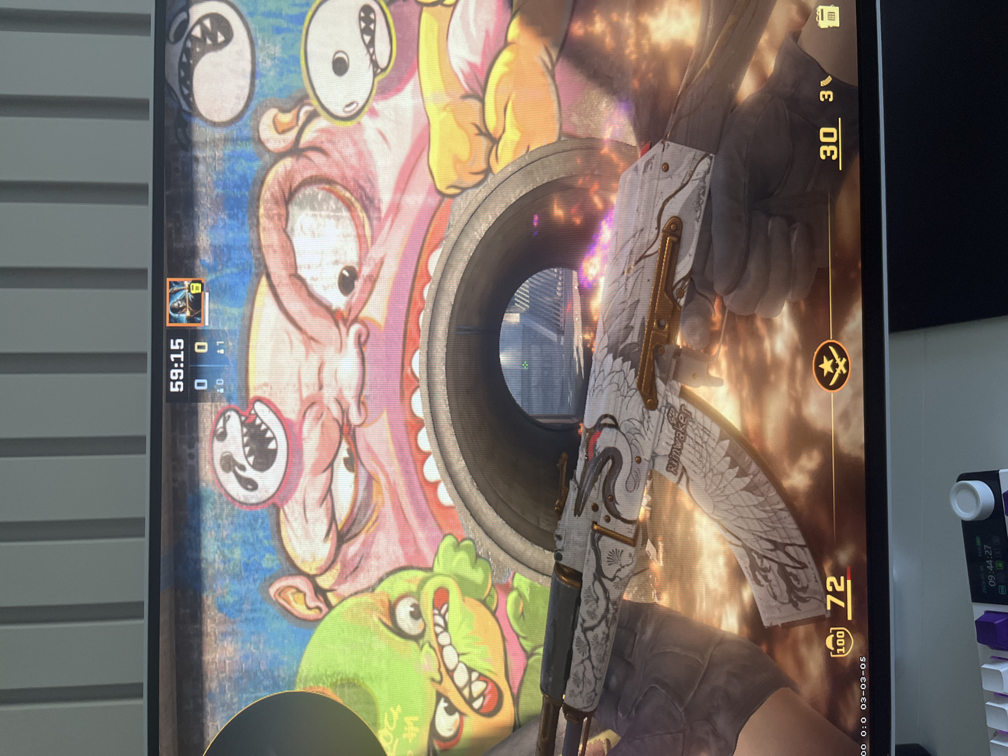 Here's a forensic description of the image:
**Scene:** A person is playing Counter-Strike: Global Offensive (CS:GO) on a computer. The game shows a first-person view of a character holding a white AK-47 skin, specifically the "Rainwaker" variant.
**Environment:** The game environment depicts a mural-covered wall adjacent to a pipe or tunnel, visible through which is a cityscape. The user interface displays game stats like remaining time (59:15), score (0-0), ammo (30), and health (72). The cityscape visible through the tunnel suggests the game is likely set in a real-world or a composite urban environment.
**Objects:** The main objects are the computer screen displaying the game, the AK-47 "Rainwaker" skin, and the game user interface. Other objects include a partial view of a keyboard and what appears to be a desk with miscellaneous items.
**Location Hypothesis:** Given the "Rainwaker" skin's association with Varna, Bulgaria, it is hypothesized that the location in the CS:GO game is based on or inspired by Varna, Bulgaria. This cannot be explicitly confirmed without further contextual clues within the game itself.