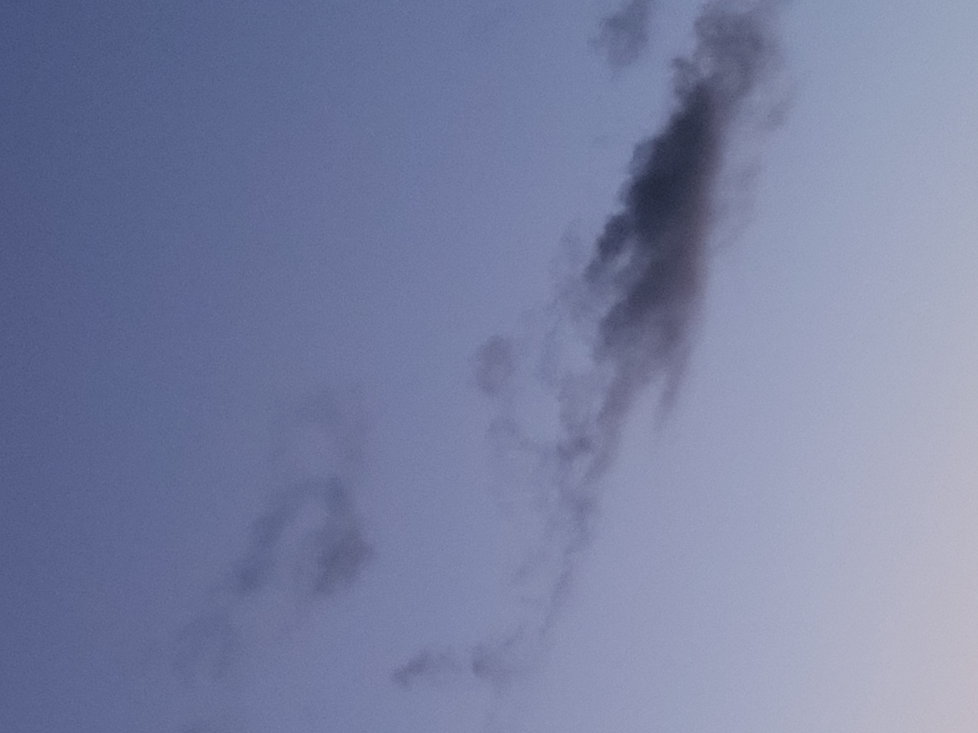 The image shows a twilight sky with scattered, wispy clouds against a pale blue gradient. There are no discernible elements of the city of Ozolnieki, Latvia, visible in the frame. The photograph is focused on the atmospheric conditions rather than any specific terrestrial location.