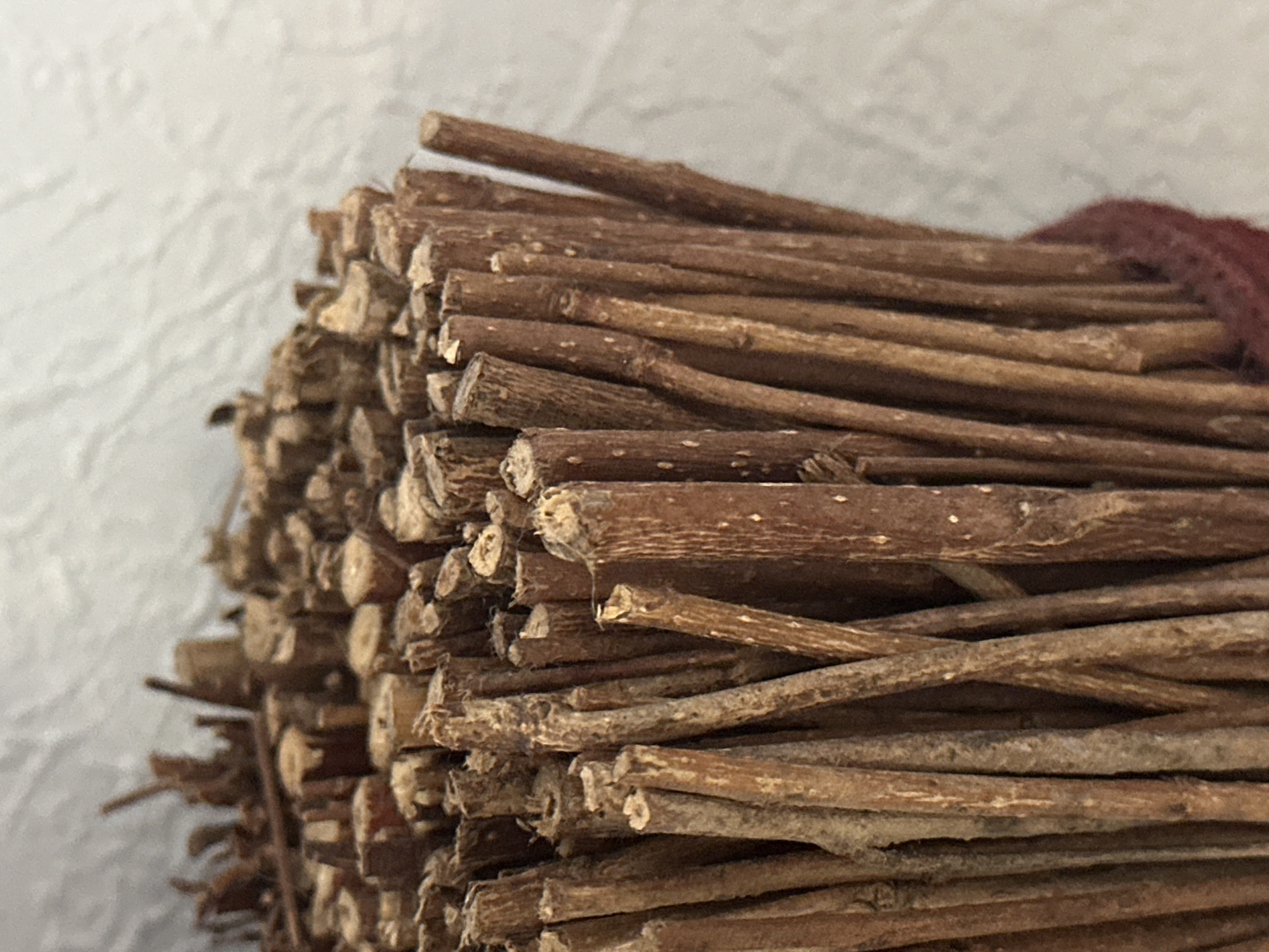 The image shows a close-up of a bundle of dried twigs. The twigs are of varying thicknesses and are tied together with a dark red material at the bottom. The background is a textured, light-colored surface, possibly a wall. There are no people or animals visible in the image. The location in the city of Nevinnomyssk, Russia is not discernible from the image itself.