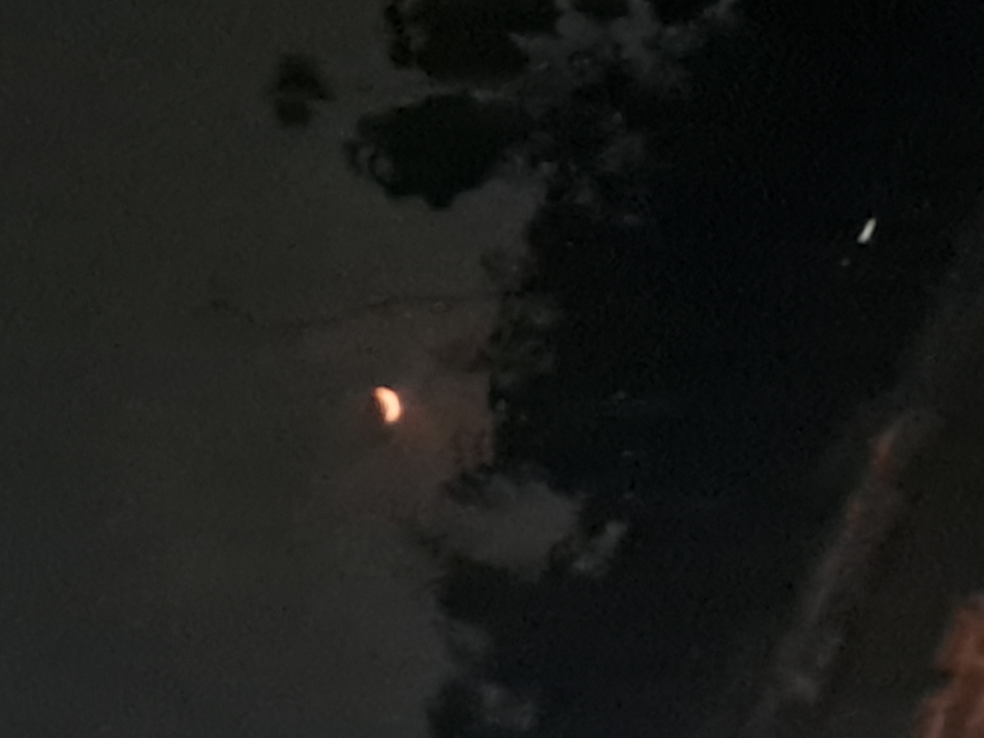A crescent moon is visible in a dark, cloudy sky. The moon is partially obscured by clouds, giving it a soft, diffused glow. The clouds are dark and dense, obscuring most of the sky. The image appears to have been taken at night, as the sky is dark and the moon is the primary light source. There are no visible people, structures, or any identifying landmarks that would suggest a specific location within Sumberejo, Indonesia. The image is abstract and focuses solely on the celestial body and atmospheric conditions.
