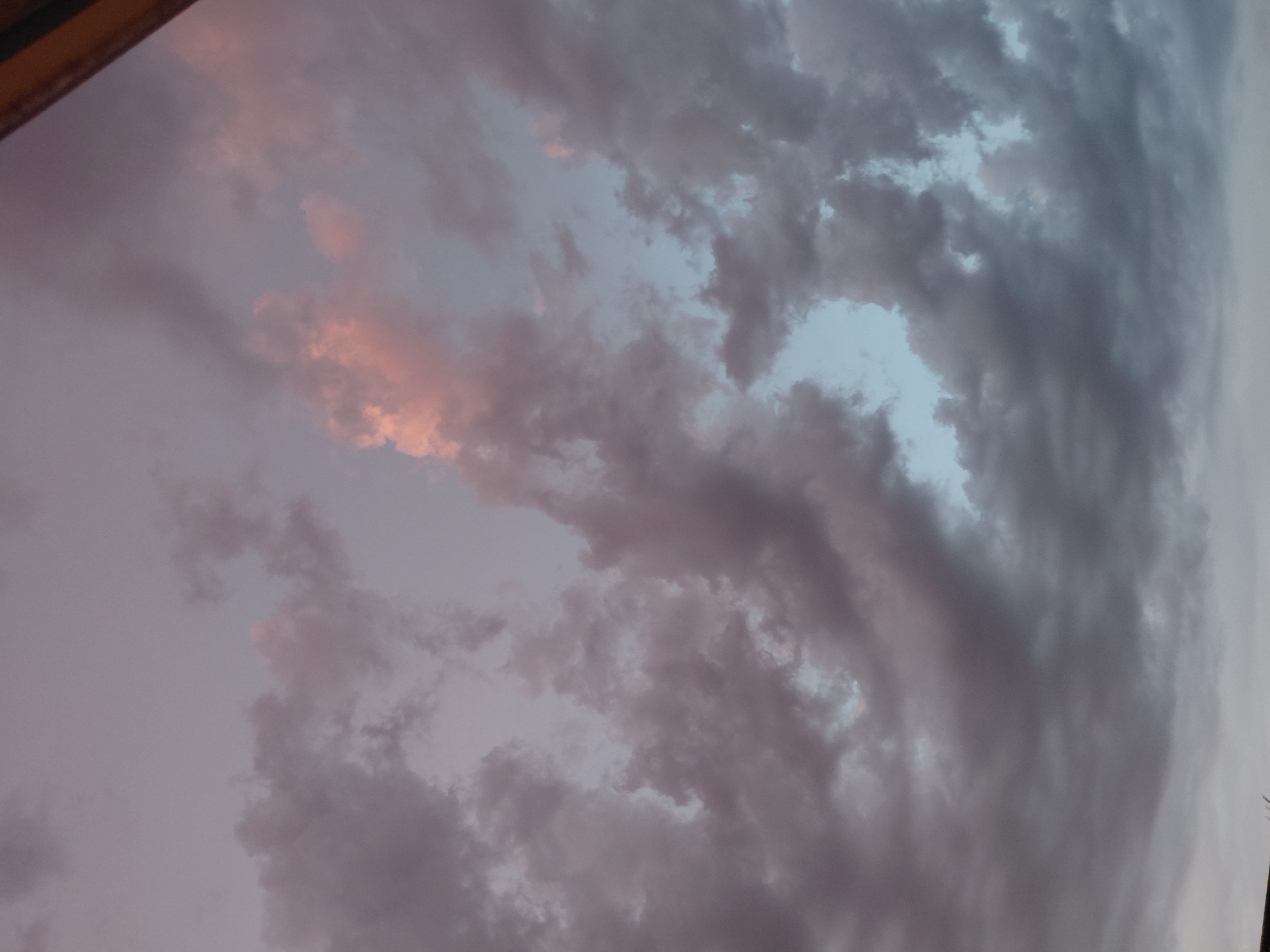 This image shows a cloudy sky with muted colors, possibly during twilight or a very overcast day. The clouds are dark gray and purplish, with hints of pink and light blue peeking through in some areas. The scene is an exterior shot, focusing solely on the sky. There are no people, subjects, objects, or actions visible in the image. The composition is abstract, emphasizing the texture and color of the clouds. The image does not contain enough information to determine its specific location in Ecublens, Switzerland.