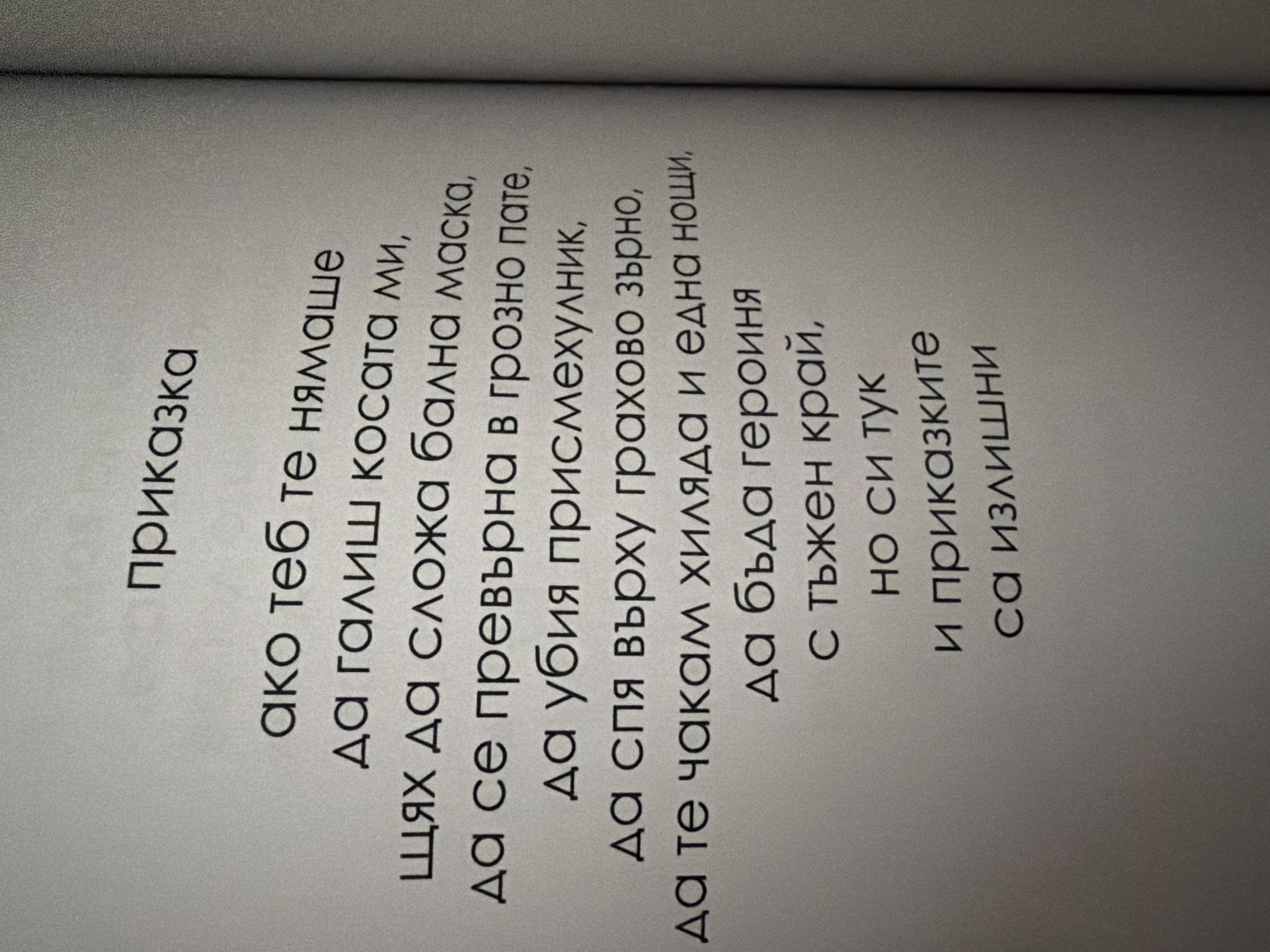 The image shows a page from a book with text printed on it. The text is in Bulgarian and appears to be a poem or a story. The page is off-white and the text is in a dark, sans-serif font. The lighting suggests the book is open and placed on a flat surface, likely indoors. There is no indication of any specific location in the city of Pazardzhik, Bulgaria, or any people, subjects, objects, or actions in the image beyond the book and its text. The environment is a plain, neutral background, typical of a printed page.