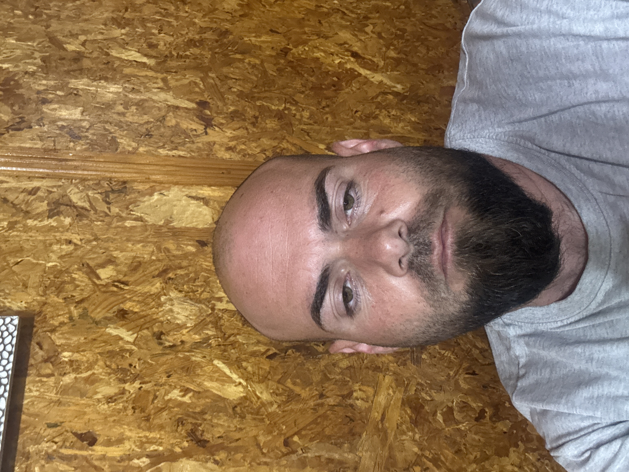 A close-up image of a bald man with a dark beard wearing a grey shirt. The background is a textured wooden surface. The location, Sarnevo, Bulgaria, is not discernible from the visual information provided.