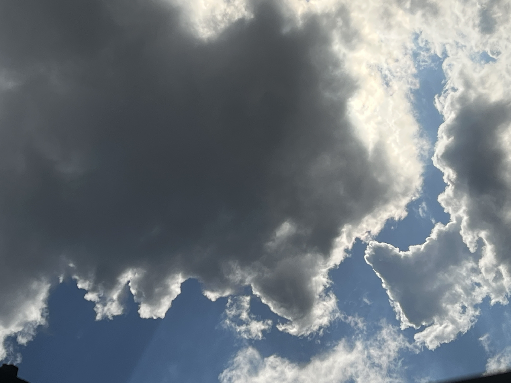 The image shows a view of a cloudy sky, with patches of blue visible between the clouds. The clouds are varied in shade, with some appearing dark and heavy, while others are lighter and more wispy. The lighting suggests it is daytime, possibly with the sun partially obscured by clouds. There are no people, animals, or man-made structures visible in this frame, focusing solely on the atmospheric conditions. The location is described as Warsaw, Poland.