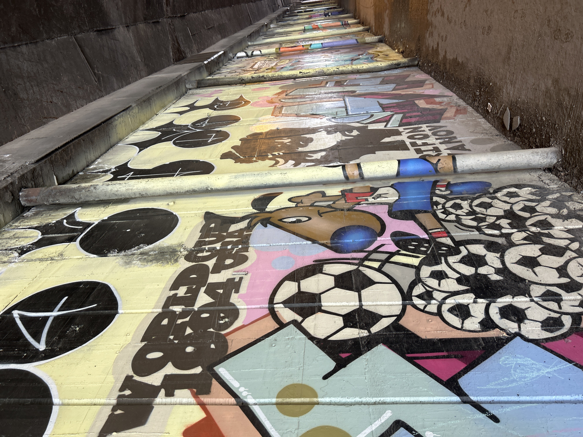The image depicts a long set of stairs covered in colorful graffiti within an urban environment. The stairs ascend into the distance, flanked by concrete walls. The graffiti art includes a variety of images, lettering, and symbols. A metal handrail runs along the side of the stairs. The location is identified as Unknown, Unknown.