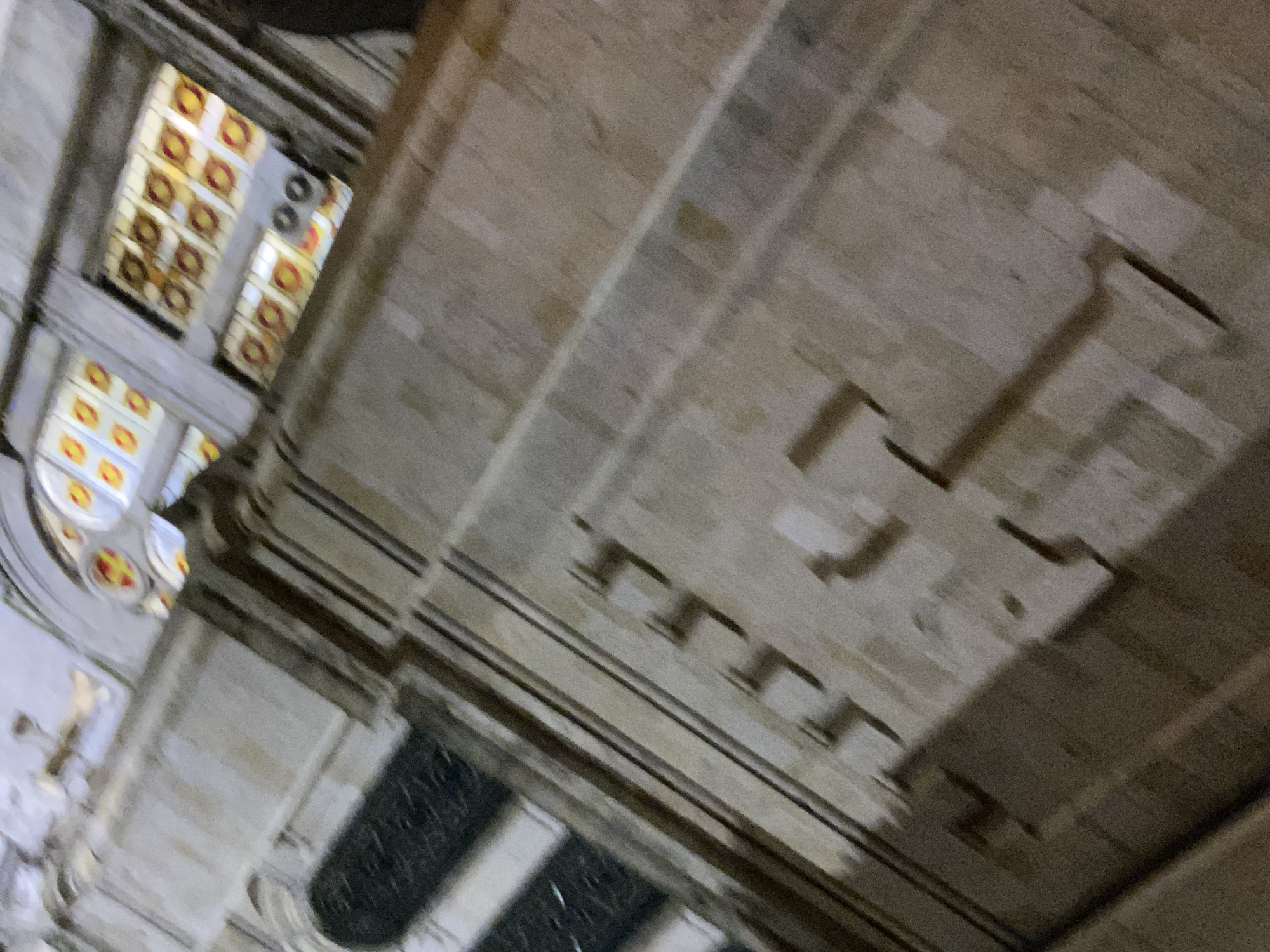The image depicts an interior architectural view with stained glass windows and stone detailing. The focus is on the building's structure, featuring multiple layers and ornamentation. While the image's orientation makes it slightly disorienting, it suggests a view of the interior ceiling of the Dormition of the Mother of God Cathedral in Varna, Bulgaria. No people are visible, and the emphasis is on the architectural elements.