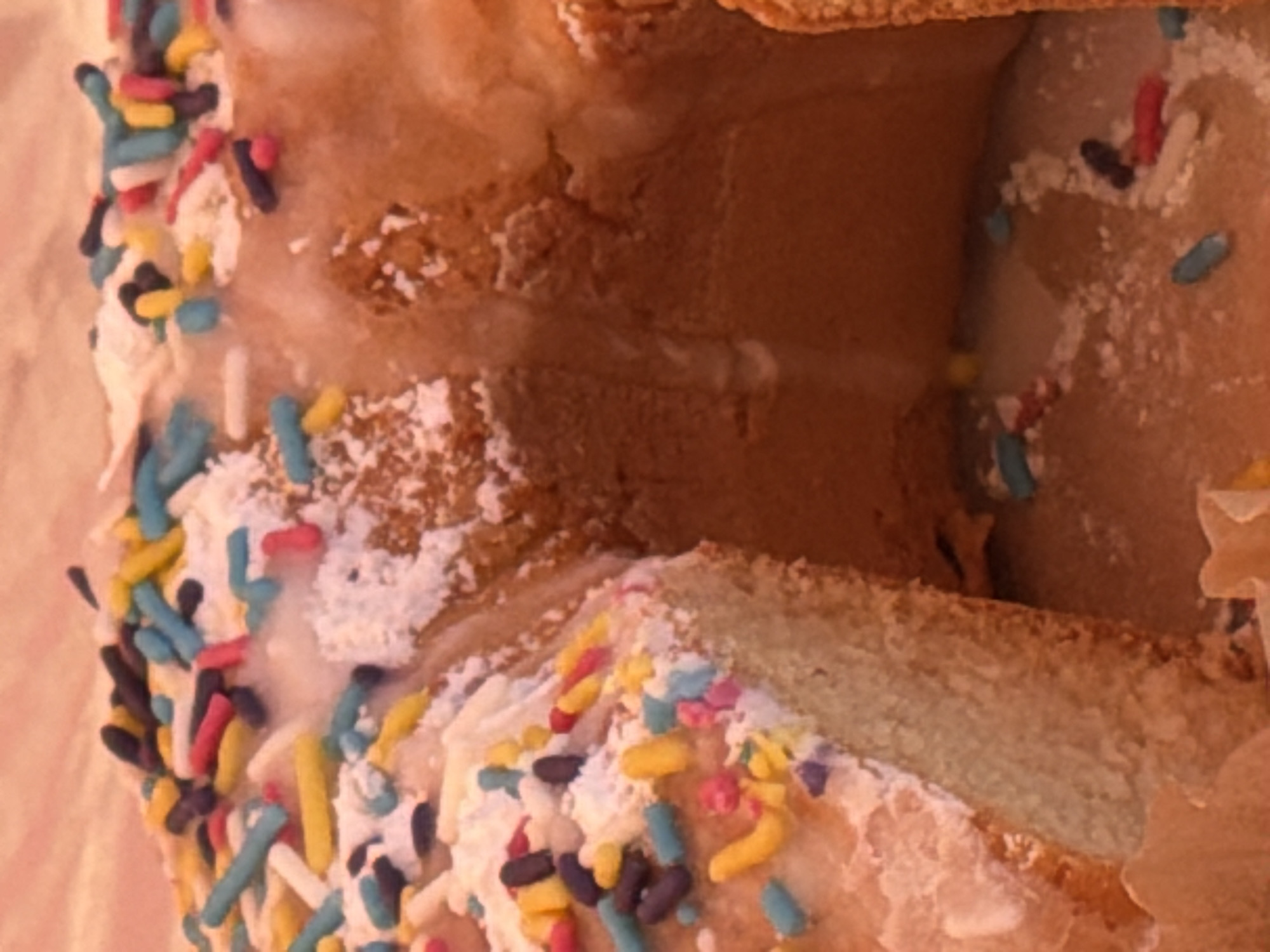 The image depicts a donut with colorful sprinkles and icing. A portion of the donut appears to be cut out, revealing the interior. There is no indication of location in Fentange, Luxembourg, people, or specific actions/interactions within the frame. The focus is solely on the donut.