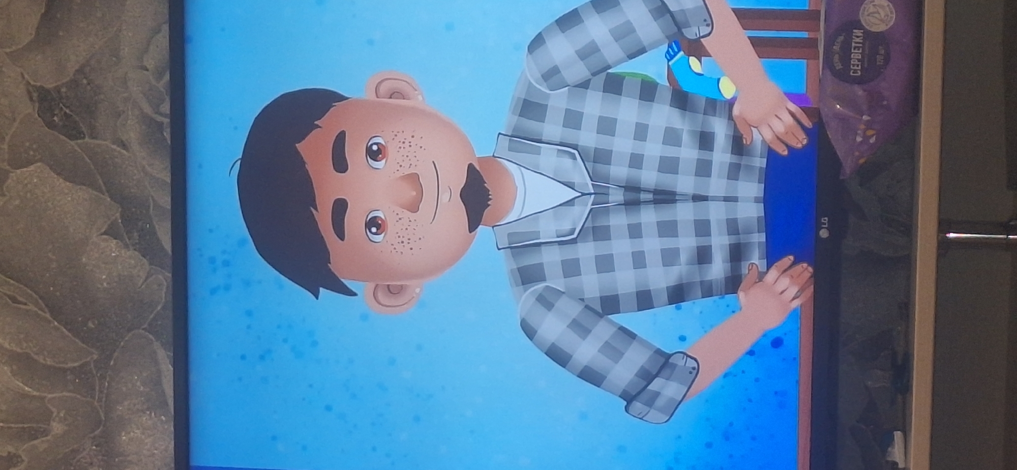 The image shows a cartoon animation of a young man with dark hair, freckles, and a goatee, wearing a plaid shirt over a white t-shirt. He has his hands on his hips and is standing in front of a blue background with scattered white speckles. Below the animation, a black LG television is visible, and on a shelf beneath the TV, a purple package with Russian text that translates to "WIPES" is partially visible. The background behind the television appears to be a textured wall. The image is not identifiable as being located in Bila Tserkva, Ukraine.