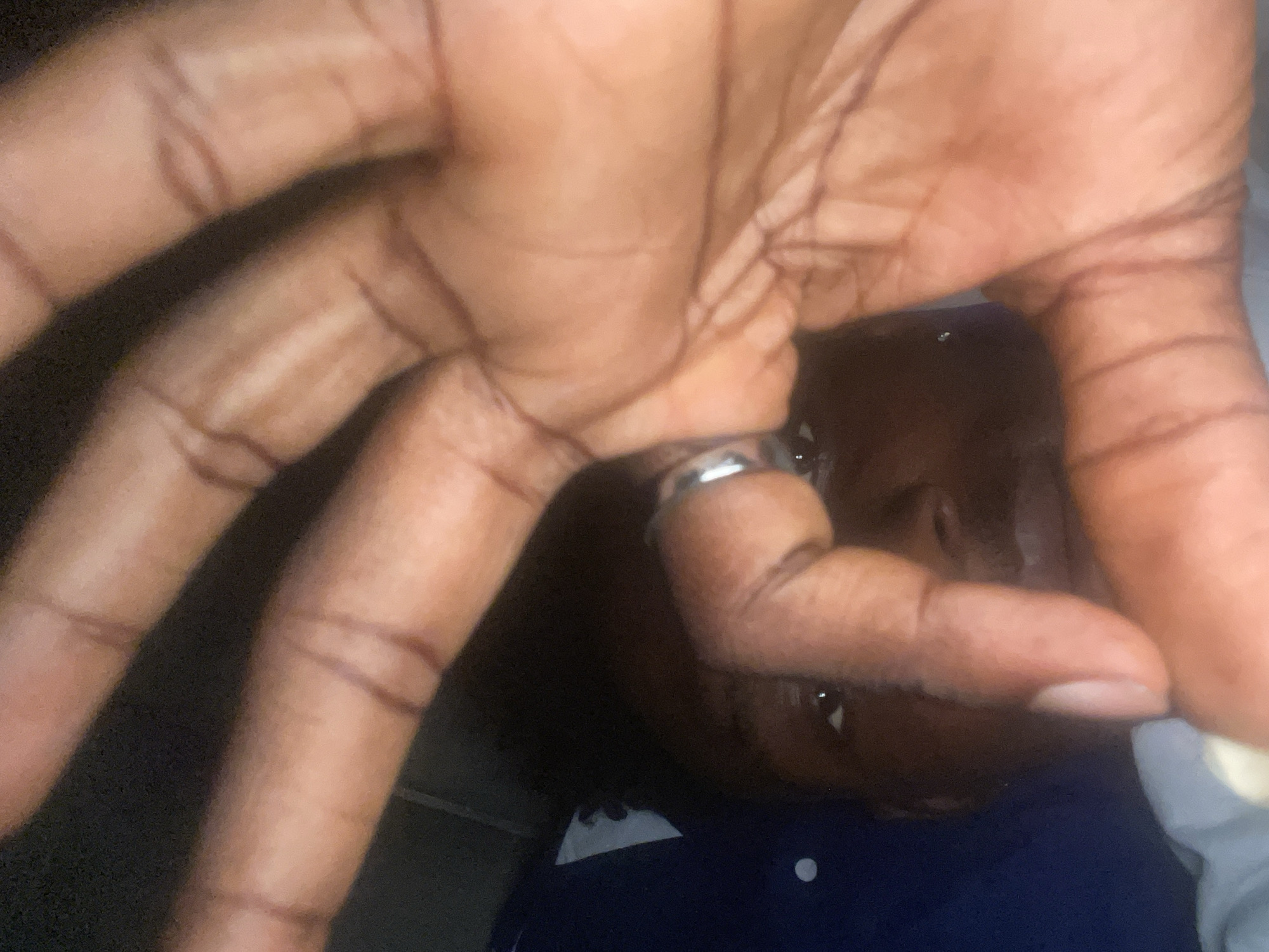 A close-up shot of a dark-skinned person's hand outstretched towards the camera, obscuring much of the face. A silver ring is visible on one of the fingers. The individual is wearing a dark blue shirt with a white collar and a single white button is visible. It is not possible to infer the location to be Lokoja, Nigeria, based on the visual information provided.