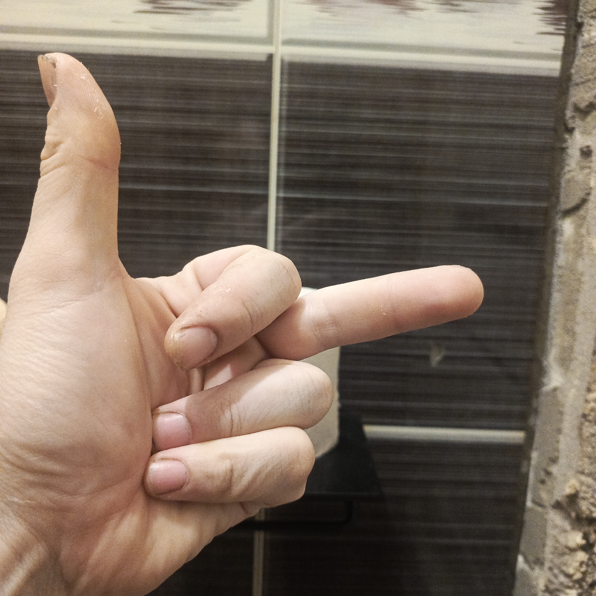 A fair-skinned hand is giving the middle finger. The background includes brown and white horizontally-striped tiles and unfinished wall construction. The location is Марковский, Russia.