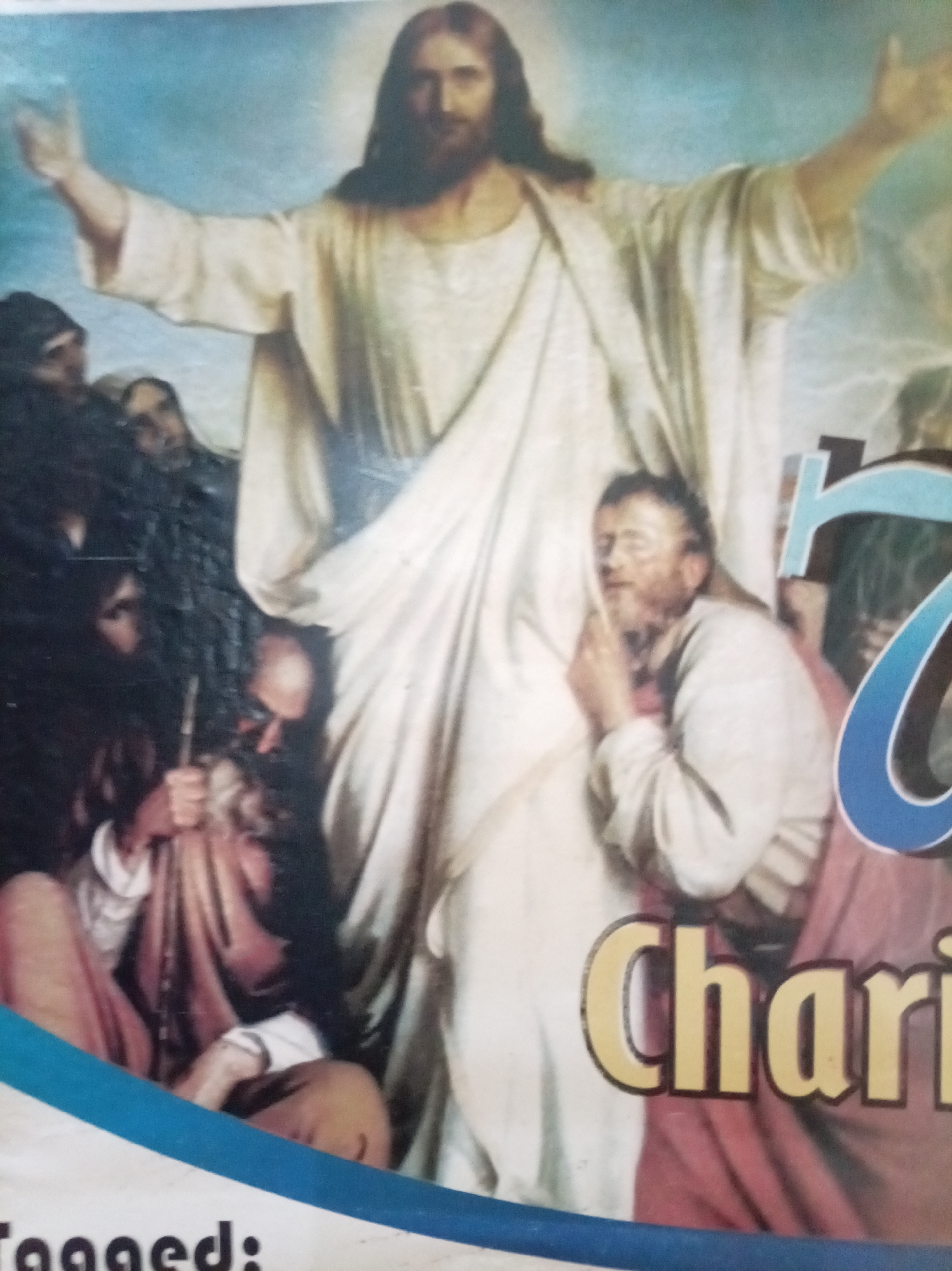The image shows a religious poster or print depicting Jesus Christ with outstretched arms, surrounded by a group of people. Text partially visible in the lower right corner reads "Char". The environment cannot be discerned and the city of Owerri, Nigeria is not evident.