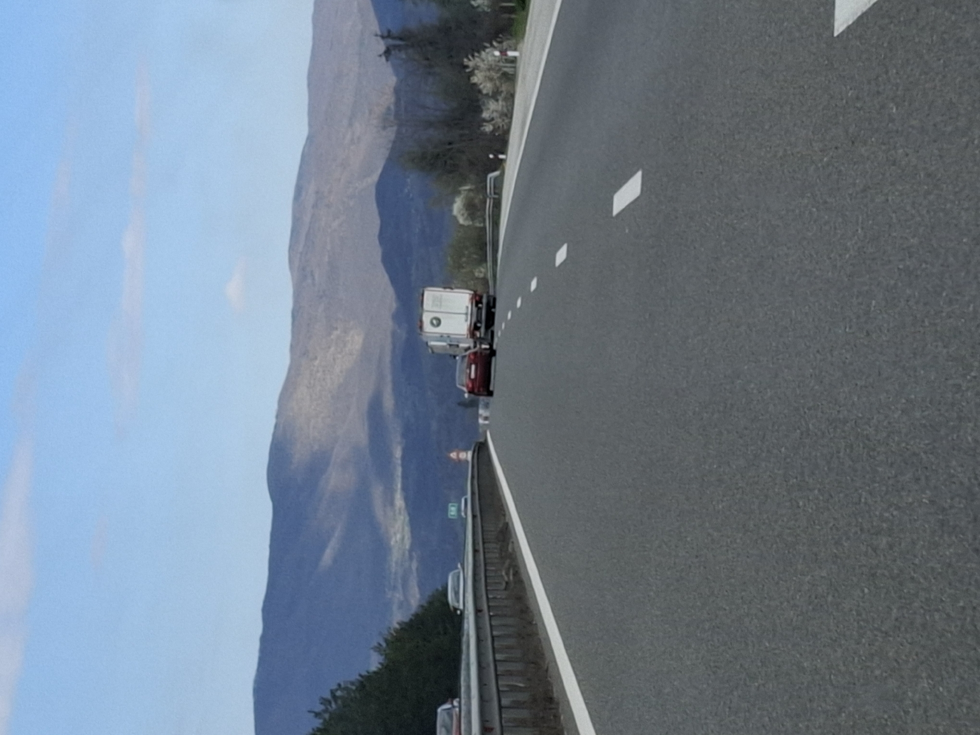 The image shows a view from a highway, likely in the vicinity of Церово, Bulgaria, given the presence of mountainous terrain in the background. A truck and a red car are visible on the road, moving in the same direction as the viewer. The highway is marked with white dashed lines and solid lines along the edge. The sky is blue with some clouds. The landscape includes trees and vegetation alongside the highway.