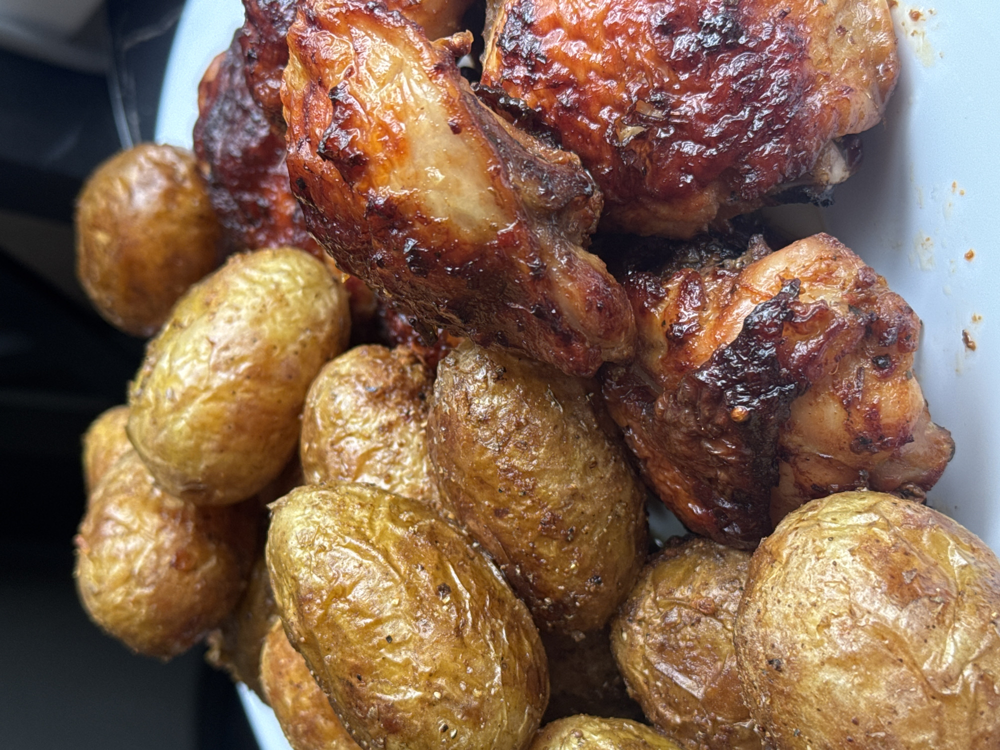 A close-up shot of a plate filled with roasted potatoes and chicken pieces. The potatoes appear to be small and round with a golden-brown color, showing signs of seasoning. The chicken is cooked to a deep brown with a glazed appearance.
The location is not discernible from the image. There is no indication of the city of Chaikovsky, Russia.