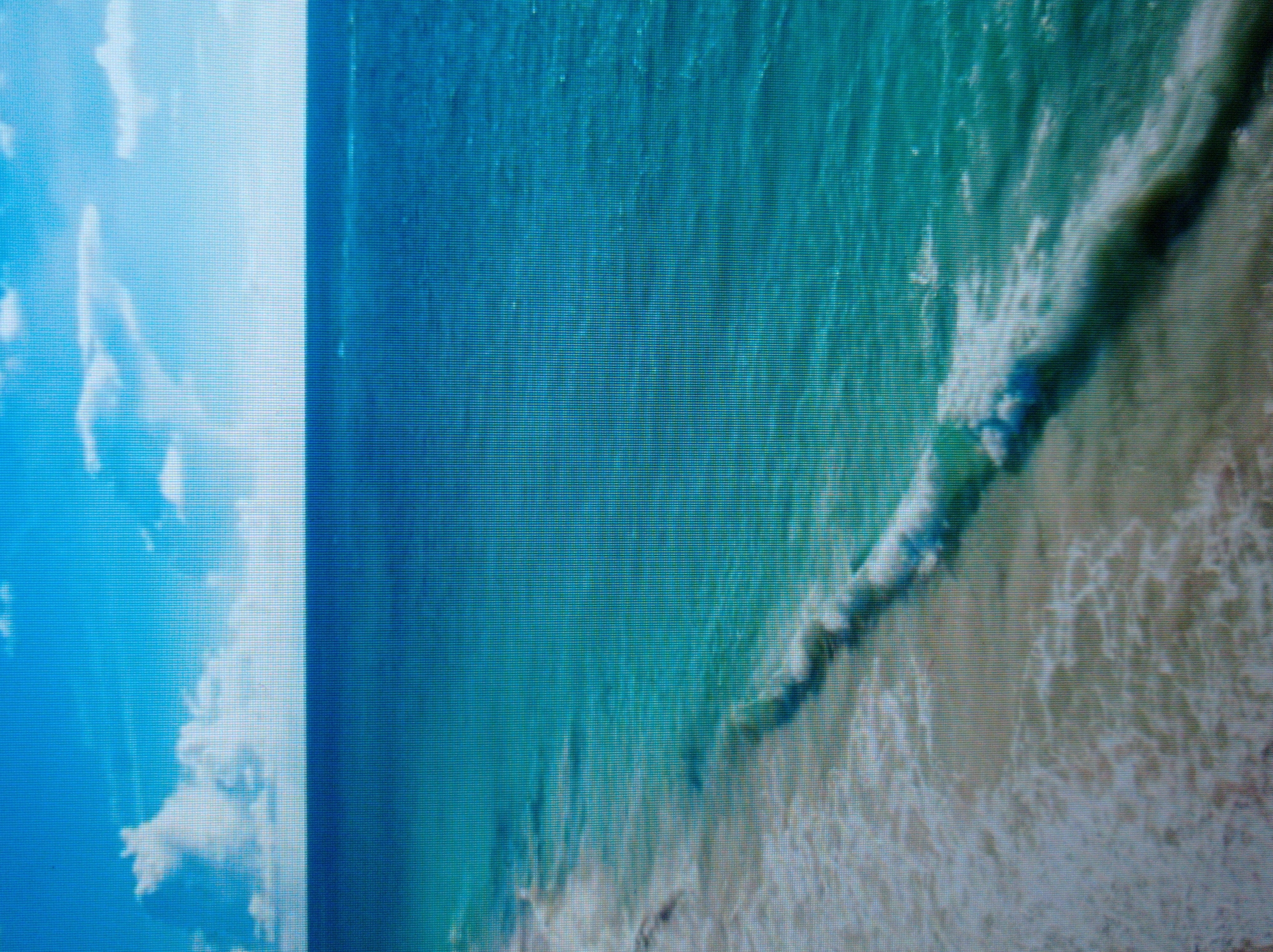 The image displays a bright, daytime scene of a tropical beach with clear blue skies and turquoise ocean water. The horizon line is visible, separating the sea from the sky. White clouds are scattered across the sky. Gentle waves are breaking on a sandy beach, with foam visible where the water meets the shore. The overall impression is one of a serene and picturesque coastal landscape. There are no people, subjects, objects, actions, or interactions depicted in the image. The location is a beach. The image does not depict the city of Mukachevo, Ukraine, as it shows a tropical beach scene.