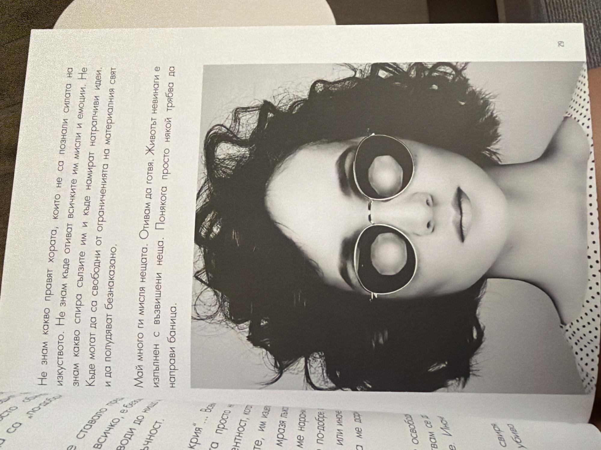 This is a close-up, black and white photograph of a book opened to a page featuring text and an image. The text on the left side is in Bulgarian. The image on the right is a portrait of a woman with dark, curly hair, wearing round, dark-lensed sunglasses and a polka-dot top. The background is plain white. There is no indication of the city of Pazardzhik, Bulgaria, or any specific location within it. The image focuses on the book's content and the printed portrait.