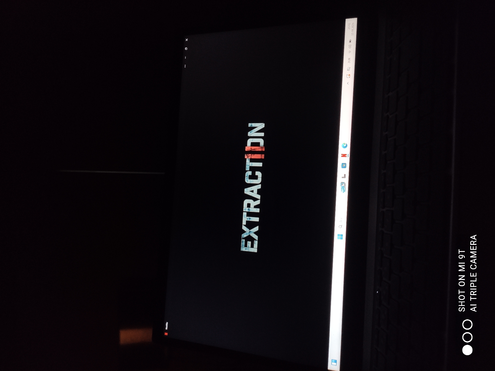 The image displays a laptop screen in a dark environment. The screen shows the title "EXTRACTION" in large, stylized white and orange letters. The Netflix logo is visible in the top left corner of the screen. The taskbar at the bottom of the screen contains icons for Windows and several applications, including a search bar and what appears to be a web browser. The keyboard of the laptop is visible below the screen, and the device is placed on a dark surface. A watermark indicating "SHOT ON MI 9T AI TRIPLE CAMERA" is present in the bottom left corner of the image. There is no indication of the city of Akçaabat, Turkey, or any people within the frame. The lighting suggests the photo was taken in low-light conditions.