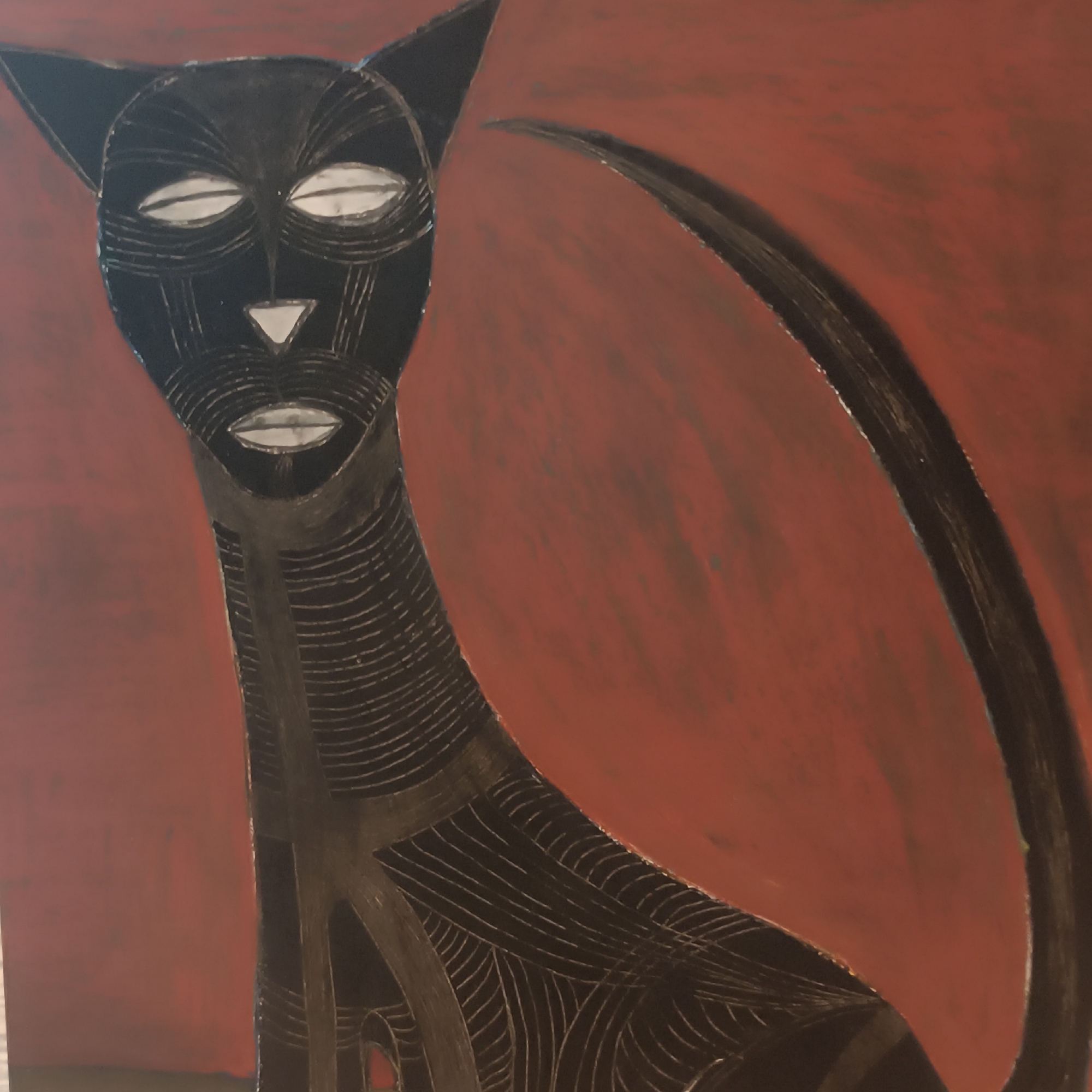 The image is a close-up of a painting of a stylized black cat against a reddish-brown background. The cat's features are exaggerated and outlined in white and black. Its eyes are large and almond-shaped with white pupils and black irises. Its nose is a white triangle. The cat's neck and body are adorned with intricate black line work, creating a textured effect. A long, curved black tail extends to the right of the cat. The painting is abstract and appears to be rendered in acrylic or oil paint, with visible brushstrokes and texture on the background. The artwork is not located in Frankfurt, Germany, or any specific city.