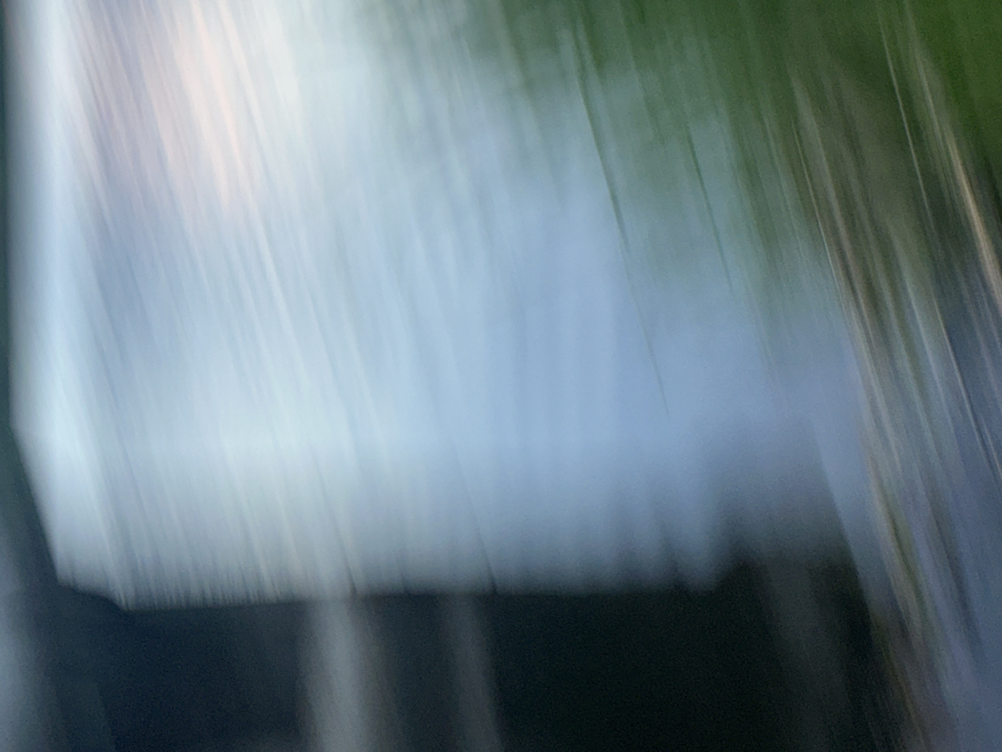 The image is blurry and out of focus, showing streaks of white, light blue, green, and dark shades. It is not possible to determine a specific location in Moscow or identify any people, subjects, objects, actions, interactions, or environmental details.