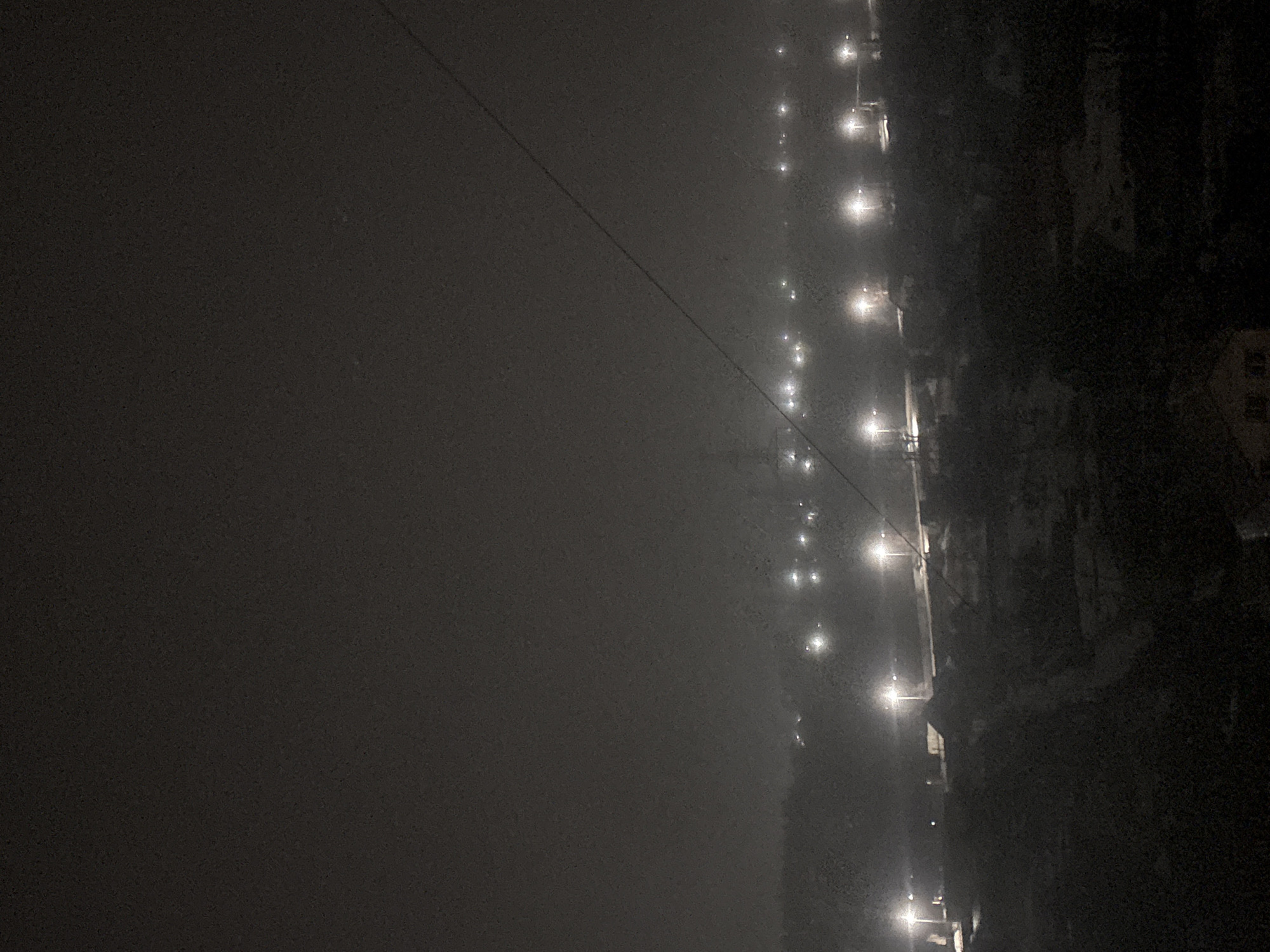 At night, the city of Chaikovsky, Russia, is obscured by heavy fog. Streetlights illuminate the scene along a road. The fog is so thick that it is difficult to see any buildings or other landmarks. The scene appears to be devoid of people.
