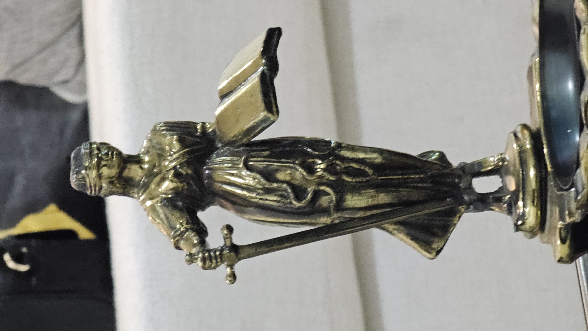 The image depicts a golden-colored statue of a figure, possibly Lady Justice, holding a sword. The statue has a blindfold or head covering and appears to be mounted on a decorative stand. The background is blurred, showing a light-colored surface. No specific location in San Bernardino Tlaxcalancingo, Mexico, can be determined from this image.