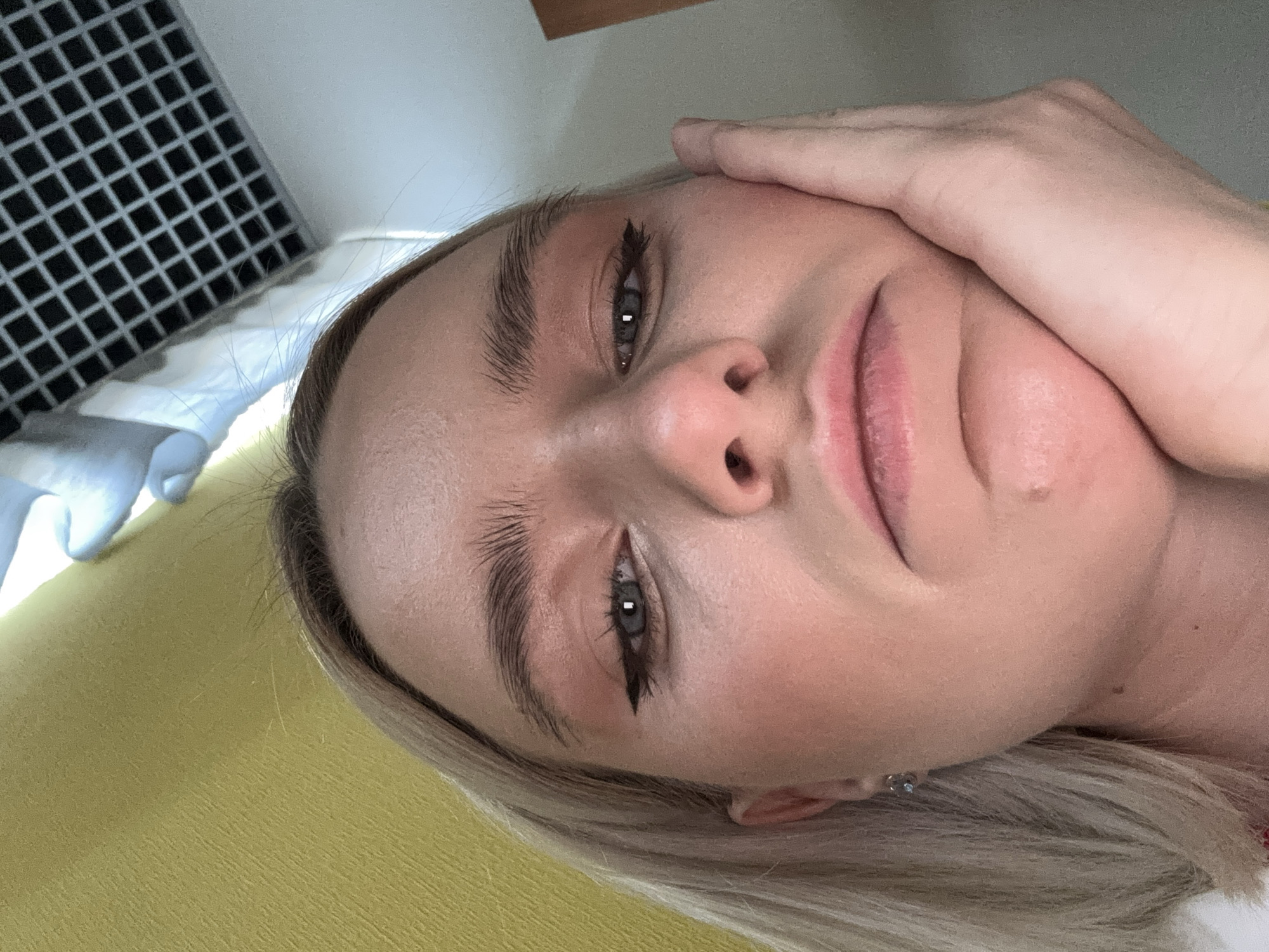 A close-up, slightly angled view of a woman's face. She has blonde hair, fair skin, and is wearing eyeliner. Her hand is touching her cheek. The background includes a yellow surface and a square grid. It is not possible to determine the location in Saint Petersburg, Russia.