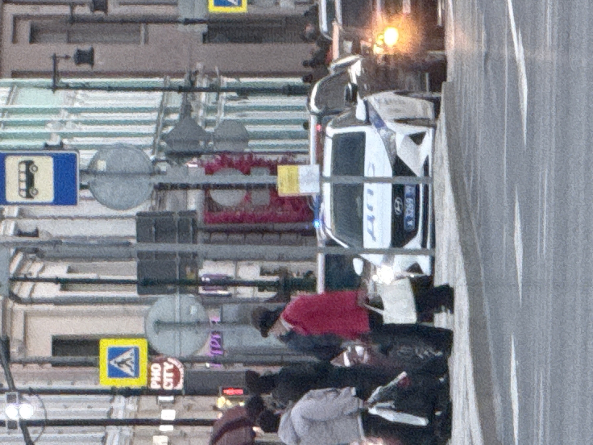 The image shows a city street scene in Moscow, Russia. Street signs for a bus stop and pedestrian crossing are visible, along with a sign indicating "Pho City". Pedestrians are walking on the sidewalk. A Hyundai police car with the license plate number X 3269 is parked at the edge of the road.