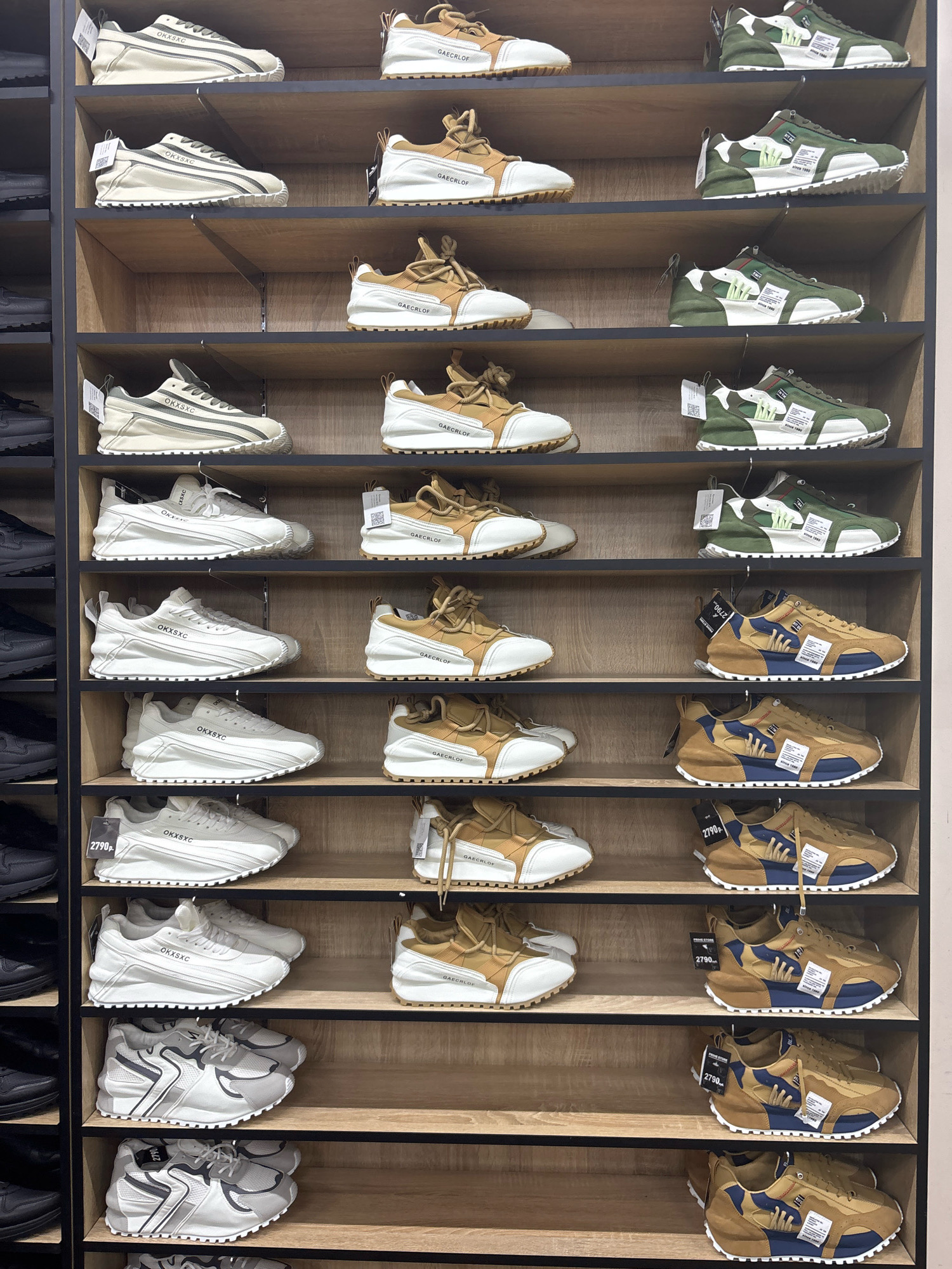 The image displays a retail store interior, likely a shoe shop, in Mytishchi, Russia. The scene is an eye-level, full-frame shot of several wooden shelves stacked with rows of athletic shoes. The shoes are primarily displayed in pairs, facing forward, with some tags and labels visible. The lighting appears to be artificial, illuminating the merchandise. There are no people visible in the image, and the focus is entirely on the arrangement of shoes on the shelves. The overall environment suggests a clean and organized retail space.