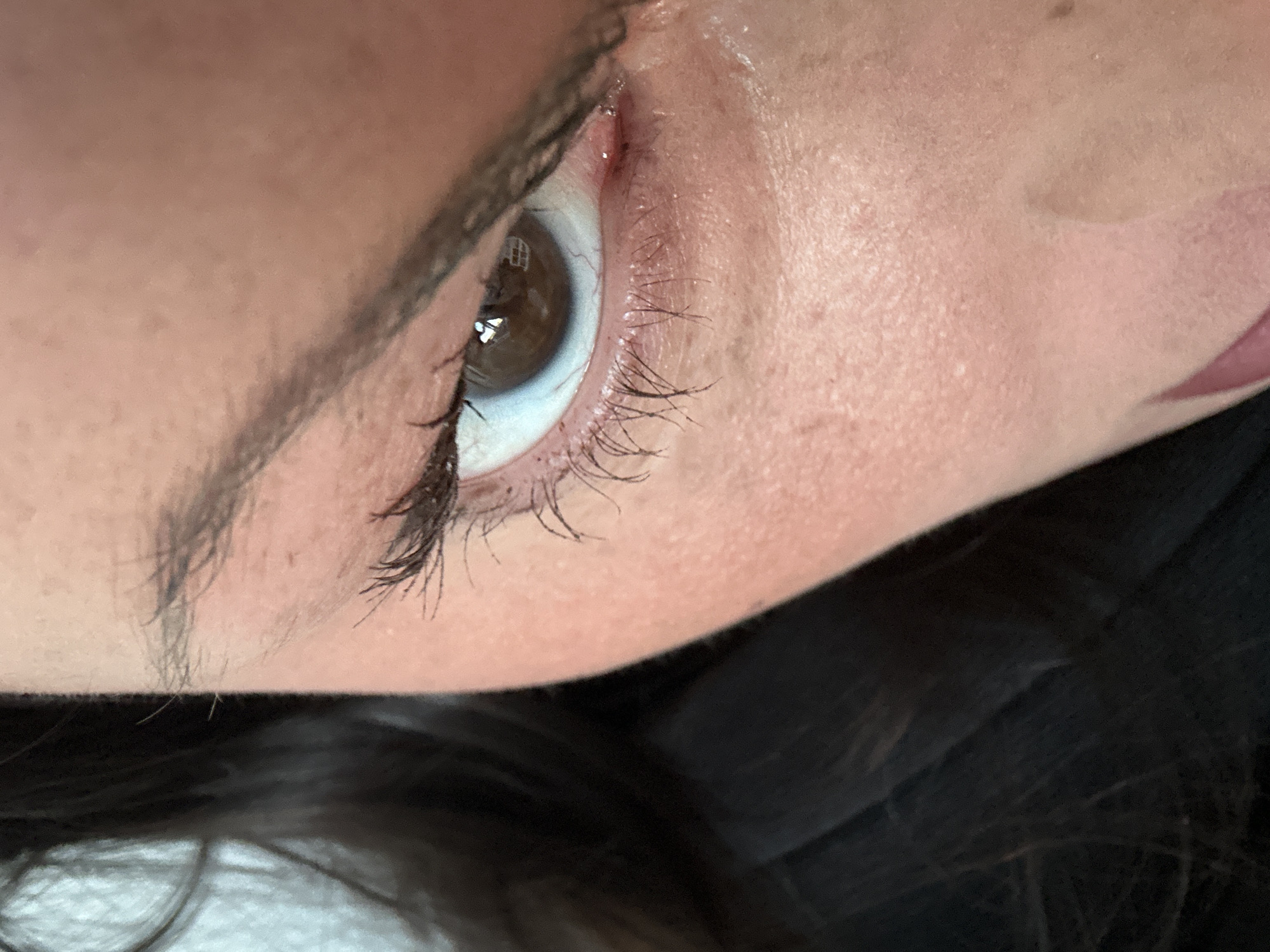 A close-up photograph depicts a human eye, angled and showing the eyebrow, eyelashes, and surrounding skin. The eye has a brown iris and a visible tear duct. The skin appears fair with some texture. The eyebrow is dark and well-defined. The lower portion of the image reveals dark hair. There is no indication of the image being in Tunbridge Wells, United Kingdom.
