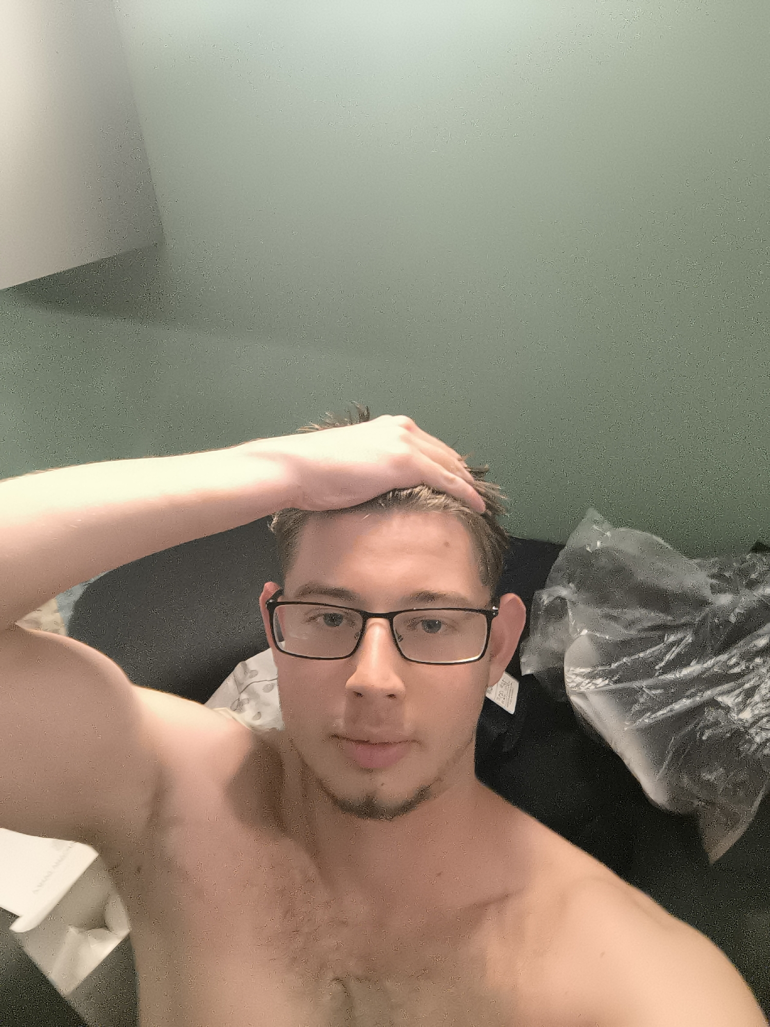 A shirtless man wearing glasses is facing the camera with his hand on his head. He appears to be indoors. No elements in the picture indicate this photo was taken in Sofia, Bulgaria.