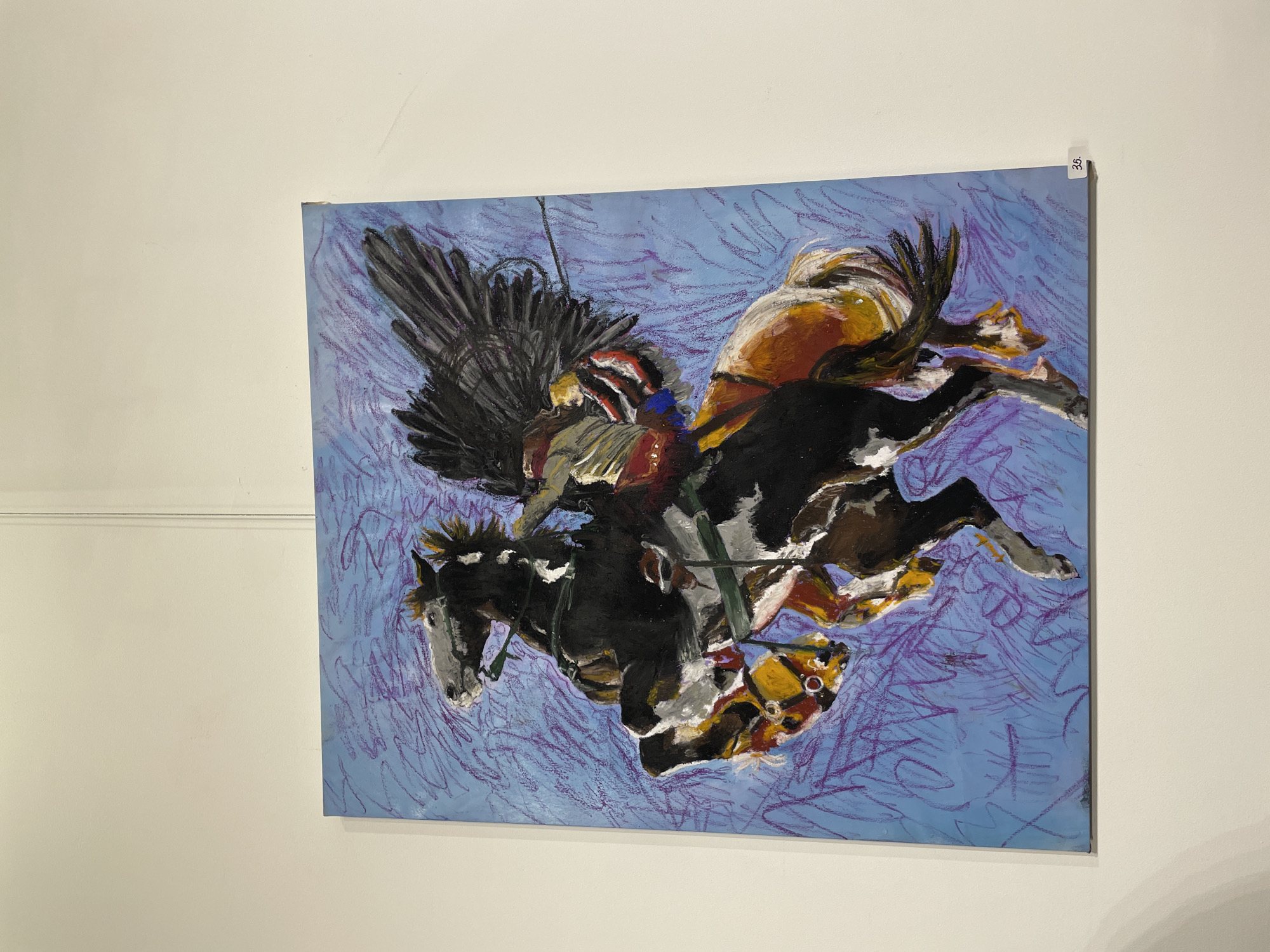 A framed painting hangs on a white wall. The painting depicts a scene with a Native American figure in a headdress riding a horse. The background is a blue color with purple scribbled lines. The horse appears to be rearing up, with its front legs in the air. The painting is attached to the wall. There is a number "36" attached to the top right corner of the painting. The location is in Plovdiv, Bulgaria.