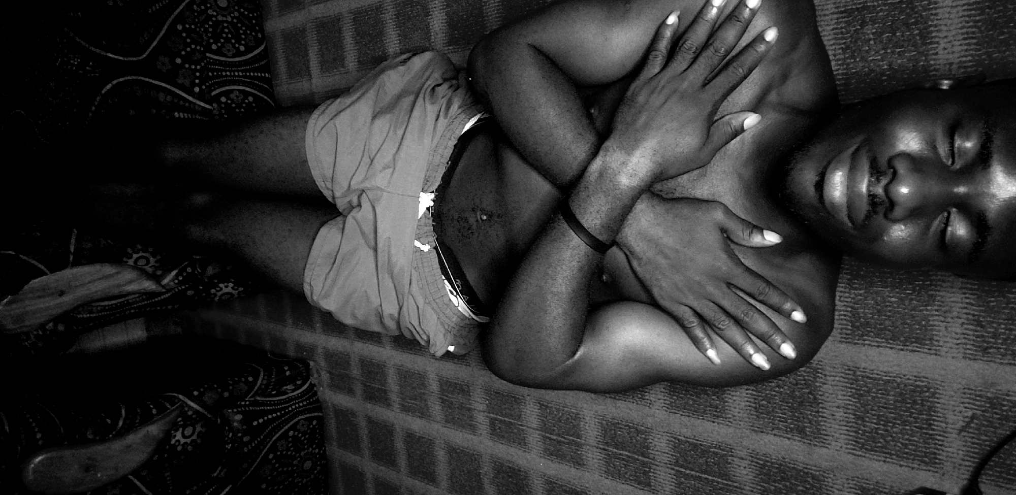 A black and white, top-down shot shows a Black man lying on a textured surface that appears to be a carpet or rug. He is wearing shorts, and his arms are crossed over his chest. The image suggests he might be lying on a bed or floor.
There is no information in the image to indicate it was taken in Narayi, Nigeria.