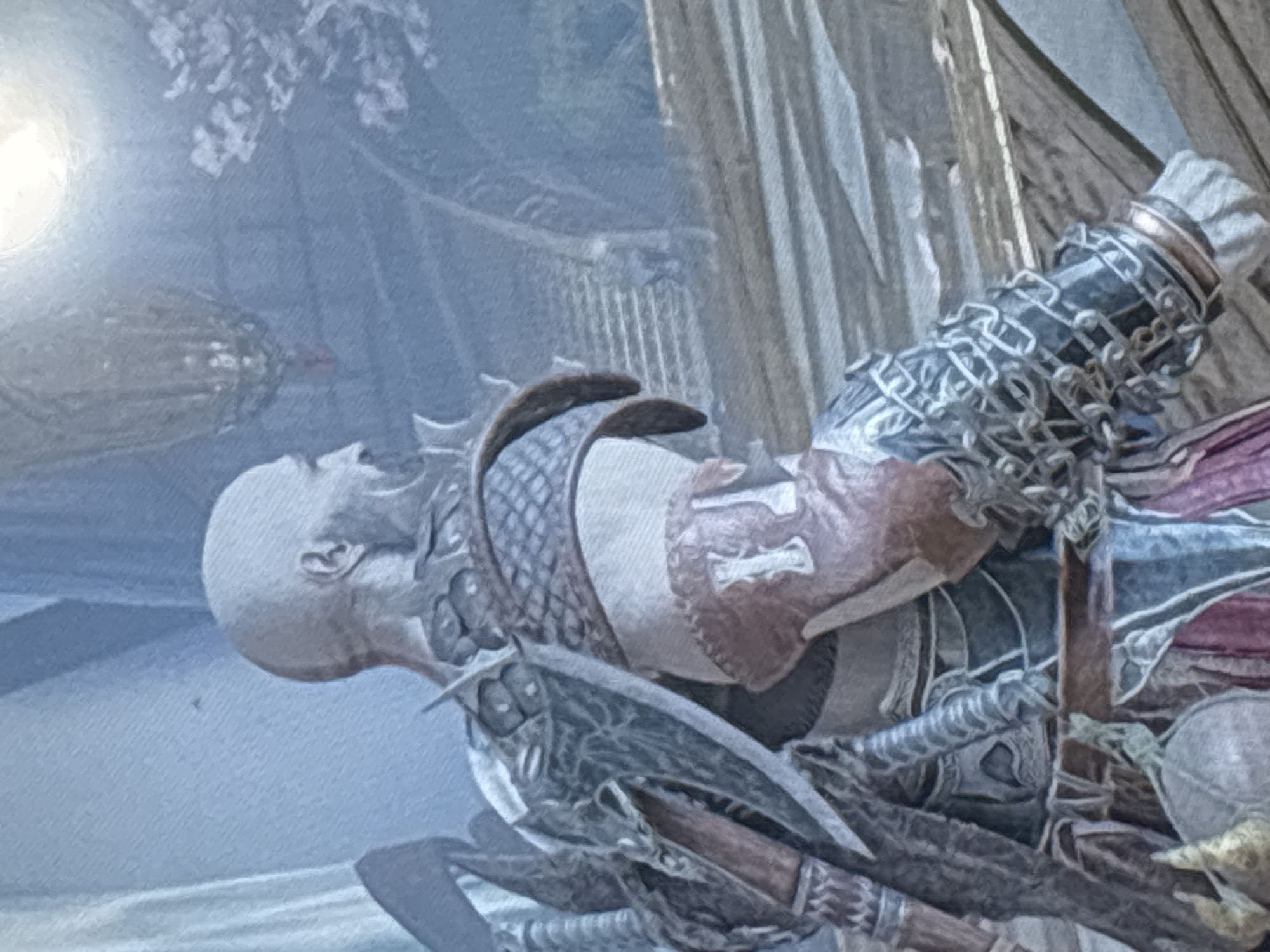 The image displays a bald, muscular individual, heavily armored, lying on their back. The character strongly resembles Kratos from the God of War video game series. Their head is tilted back, with eyes closed and mouth slightly agape, suggesting they are either deceased, unconscious, or severely injured.
The individual wears extensive armor, including a distinctive chainmail and spiked bracer on the left arm. Their torso features textured armor, possibly scale-like or woven, with some brown, leather-like components. Part of what appears to be an axe handle is visible near the hip area.
The setting appears to be outdoors or in a well-lit indoor structure, indicated by a bright light source in the upper left corner, suggesting daytime. Blurred foliage or decorative elements are visible in the upper left background. On the right side, vertical, pillar-like structures suggest an ornate building or ruins. The overall color scheme is muted, featuring cool tones of blue and grey, with earthy browns and reds in the character's attire. There is no visible text in the image. The scene evokes a sense of aftermath, defeat, or tragedy.