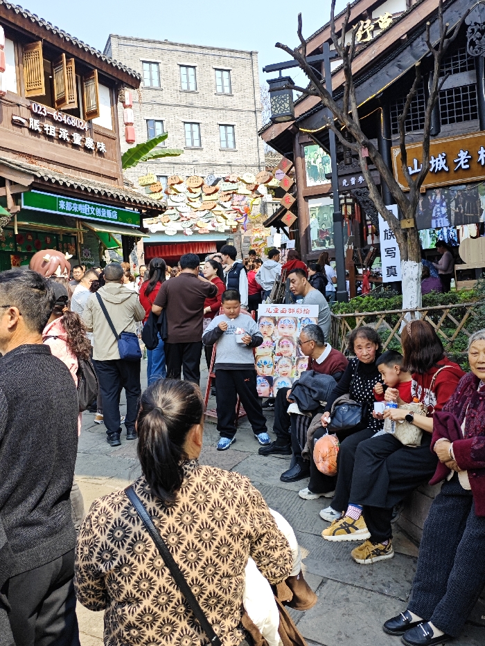 A bustling street scene in China features a mix of traditional and modern elements. Several stores line the street, adorned with Chinese characters and decorations. One store offers "Chongqing Flavor" and another is a "Creative Retail Store". Overhead, numerous decorative plaques hang in rows. Crowds of people walk around, and some rest on benches. A boy stands beside a sign depicting different face paintings. The sign reads "Children's Face Painting". A nearby sign reads "Mountain City Old Wood", and "Family Photo".