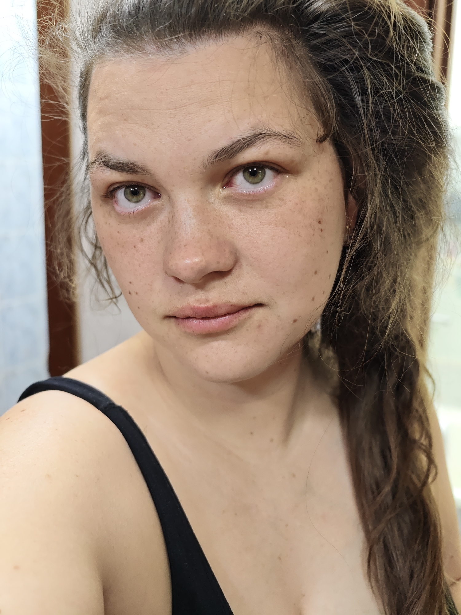 A close-up shot of a fair-skinned woman with green eyes and freckles. She is wearing a black top. Her brown hair is partially pulled back. The background is a blurred room interior. There is no indication of the location being Chaikovsky, Russia.