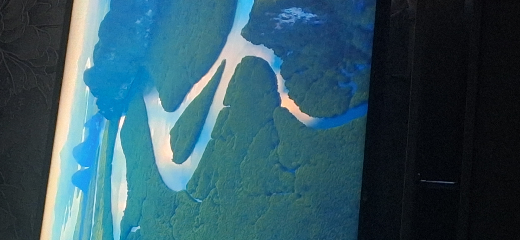 The image displays an aerial view of a winding river flowing through a lush green landscape of trees and islands. In the distance, a series of karst formations rise dramatically from the water, with some appearing as sheer cliffs and others as rounded peaks. The sky above is a gradient of blue, transitioning to a lighter hue near the horizon, with hints of sunset colors reflecting on the water's surface. The overall scene evokes a sense of natural beauty and tranquility. The image provided does not contain any information or visual cues to suggest a location in Bila Tserkva, Ukraine.